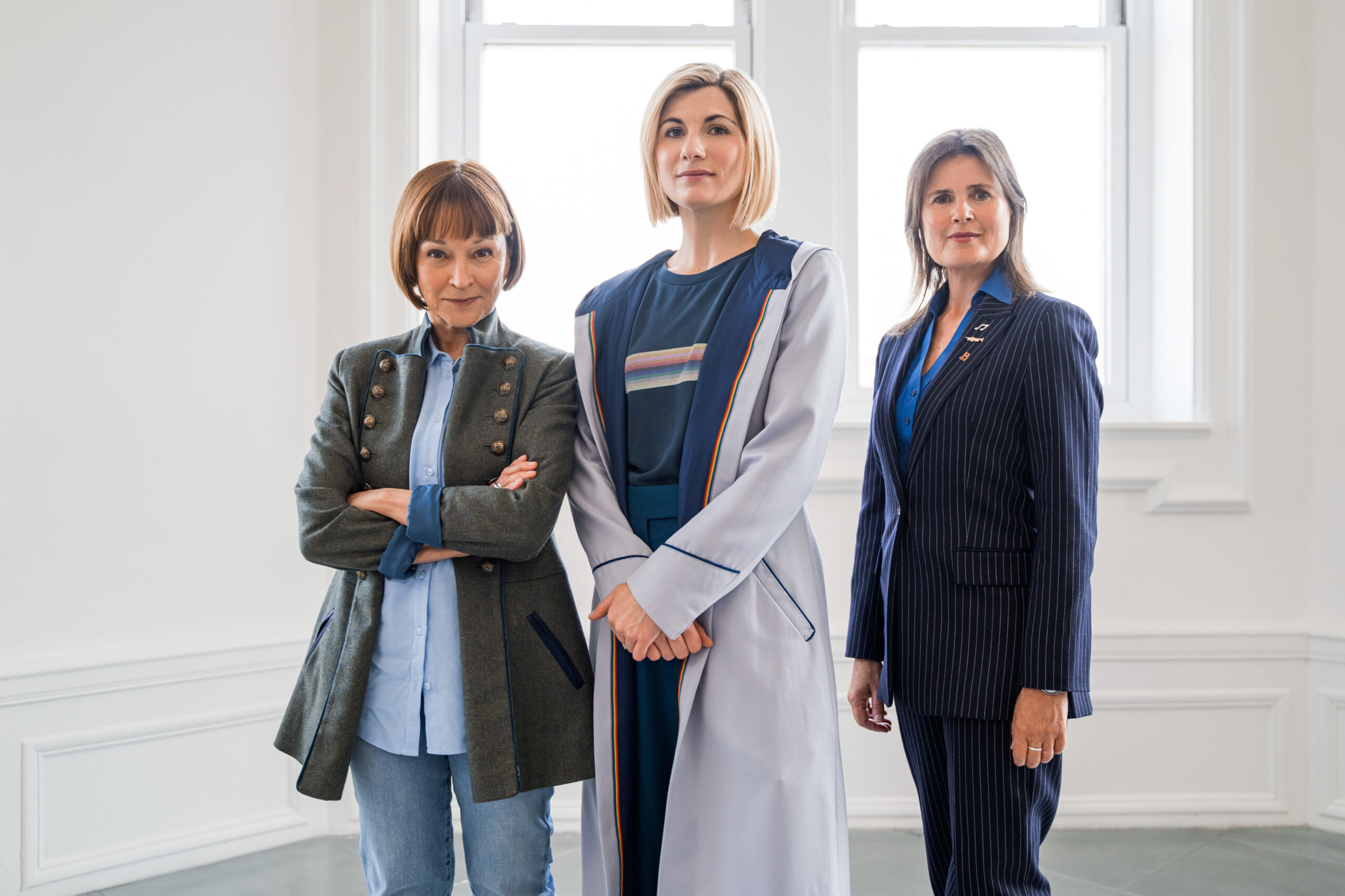 TEGAN (JANET FIELDING), The Doctor (JODIE WHITTAKER) and ACE (SOPHIE ALDRED) in Doctor Who, they stand in a line and pose with the camera