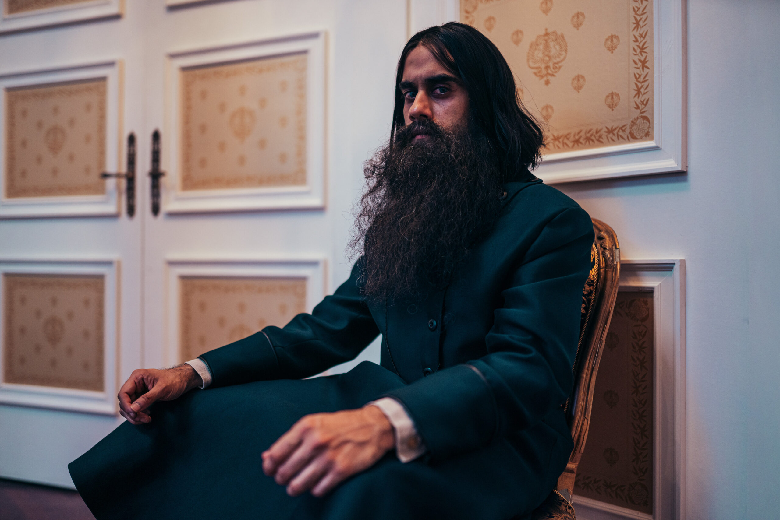 Sacha Dhawan as The Master, he has a long beard and a frown as she sits on a chair