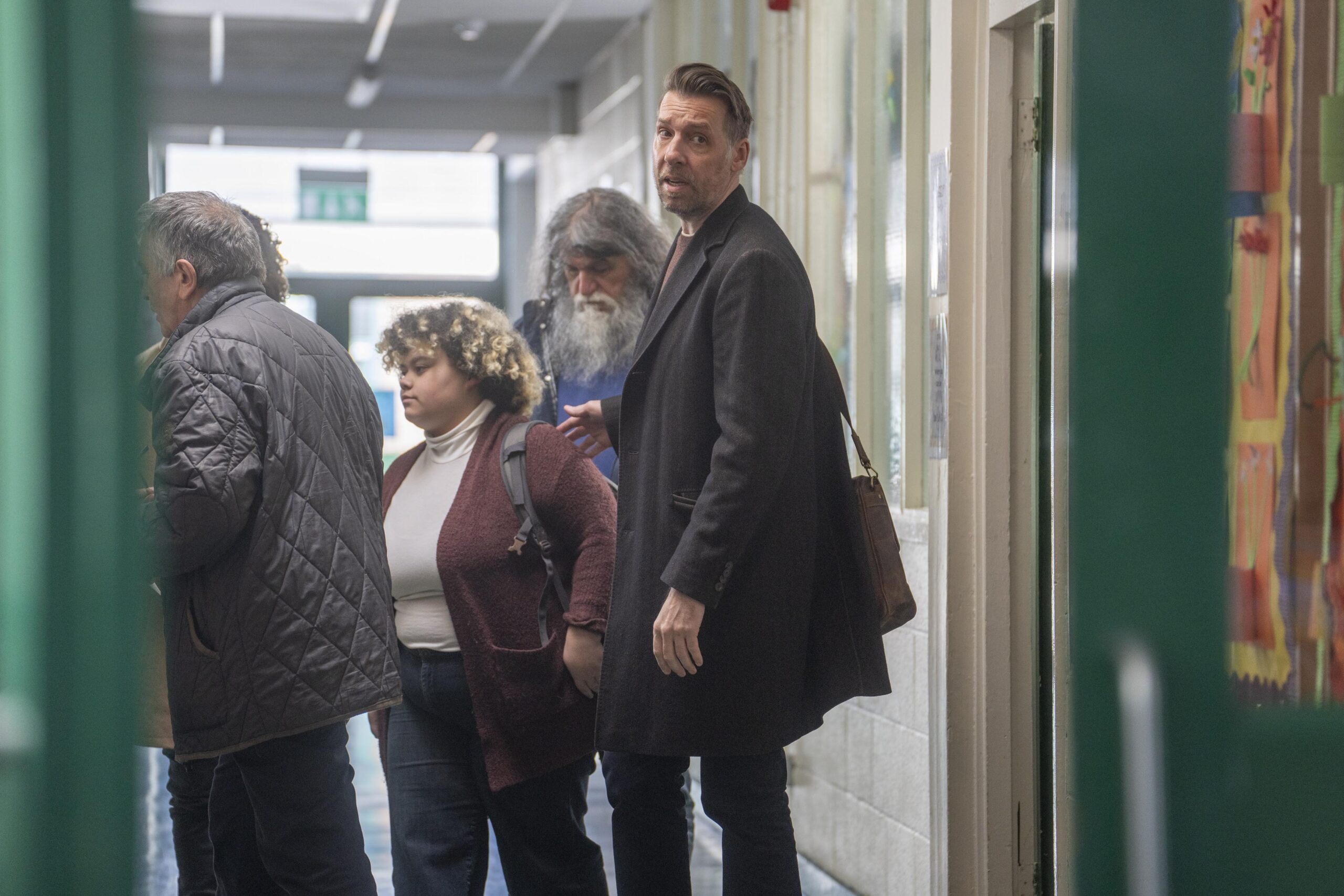 Craig Parkinson as George in The House Across The Street, looking down a hallway with a frown as his students stand behind him