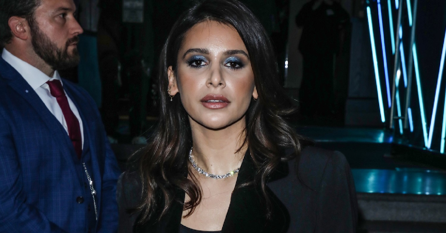 Actor Paige Sandhu on red carpet wearing a dark jacket with a bouncer in the background