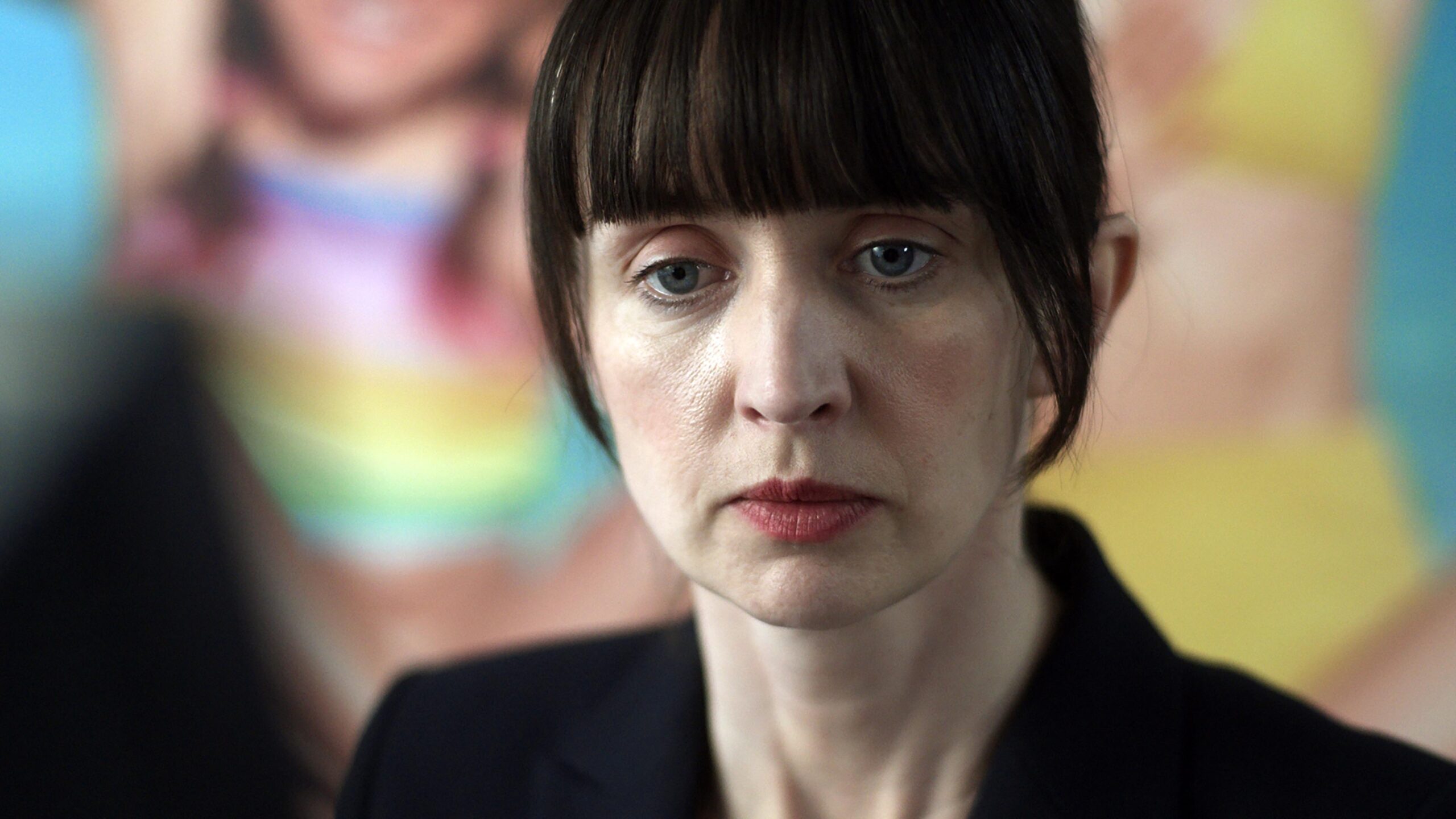 SABINE (LISA DWYER HOGG) in the house across the street, she looks down with a frown in a black suit