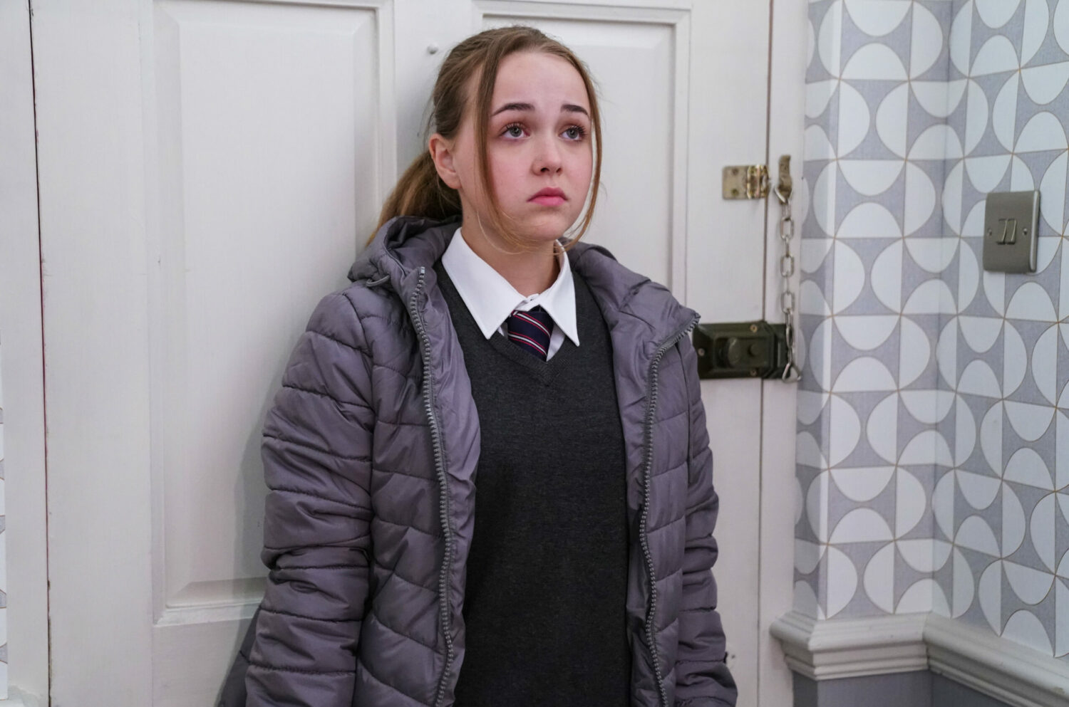 Amy Mitchell looks upset as she stands with her back to the door in EastEnders