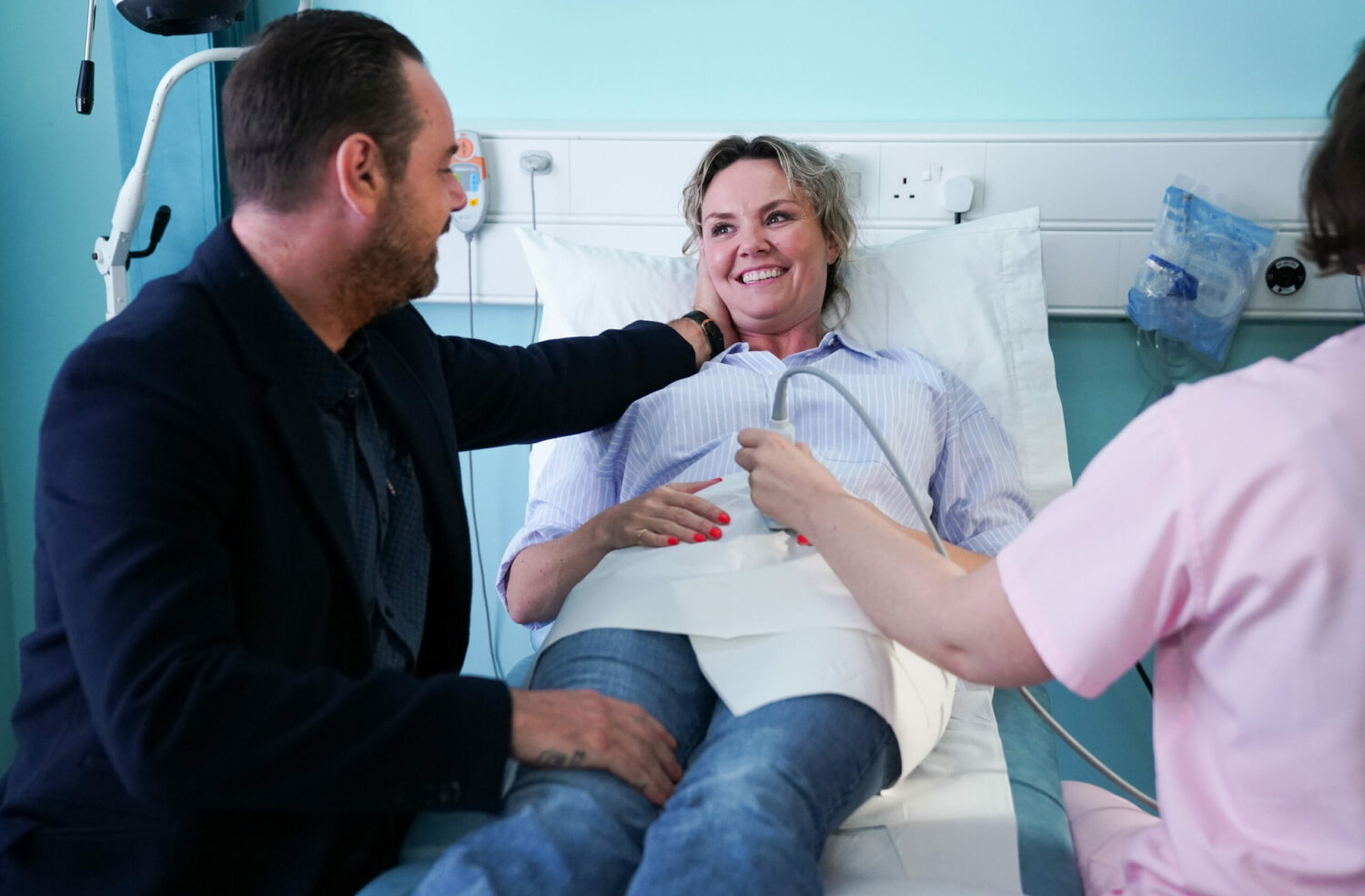 Mick and Janine smiling at the baby scan while a nurse performs an ultrasound in EastEnders