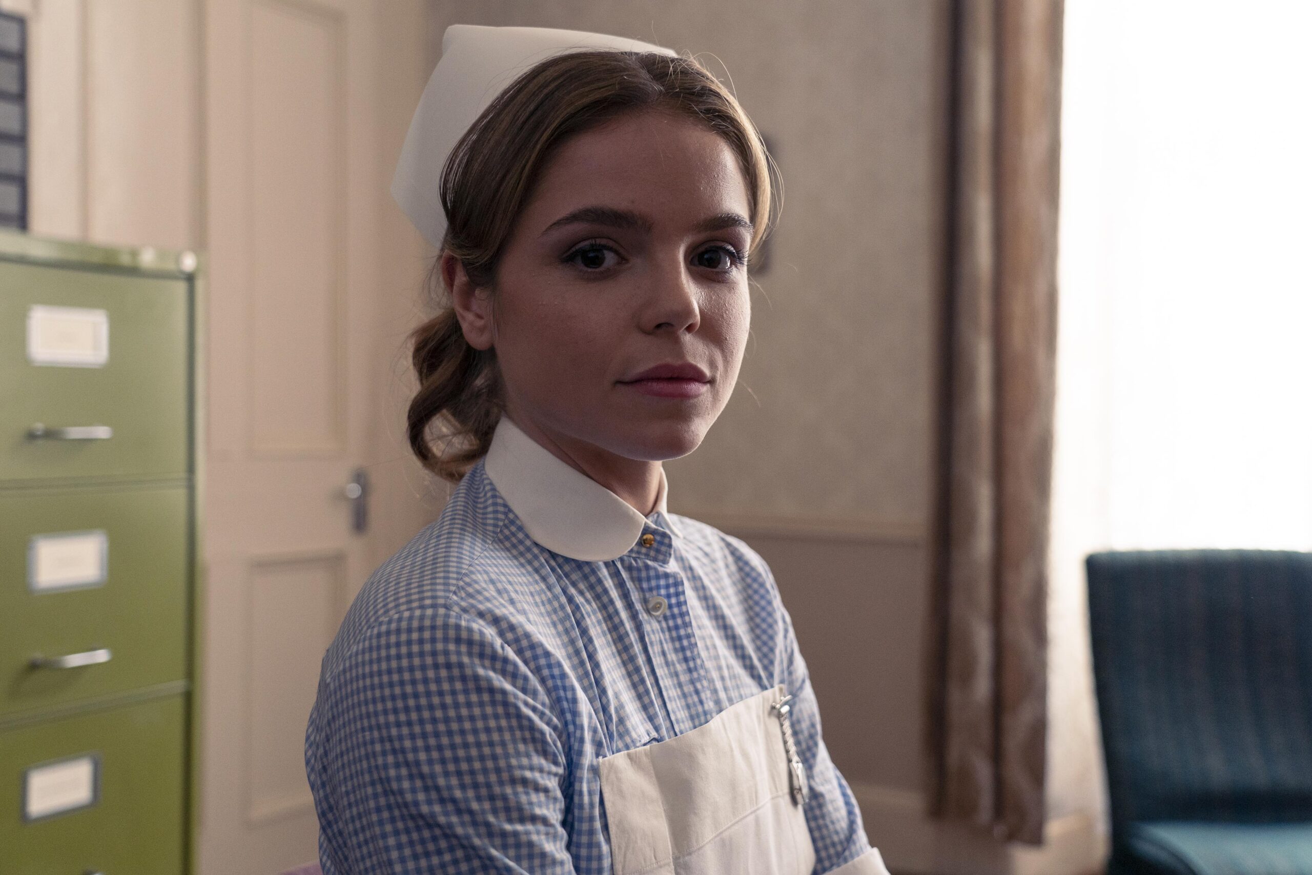 Nurse Pardoe smiles in a locker room in Dalgliesh