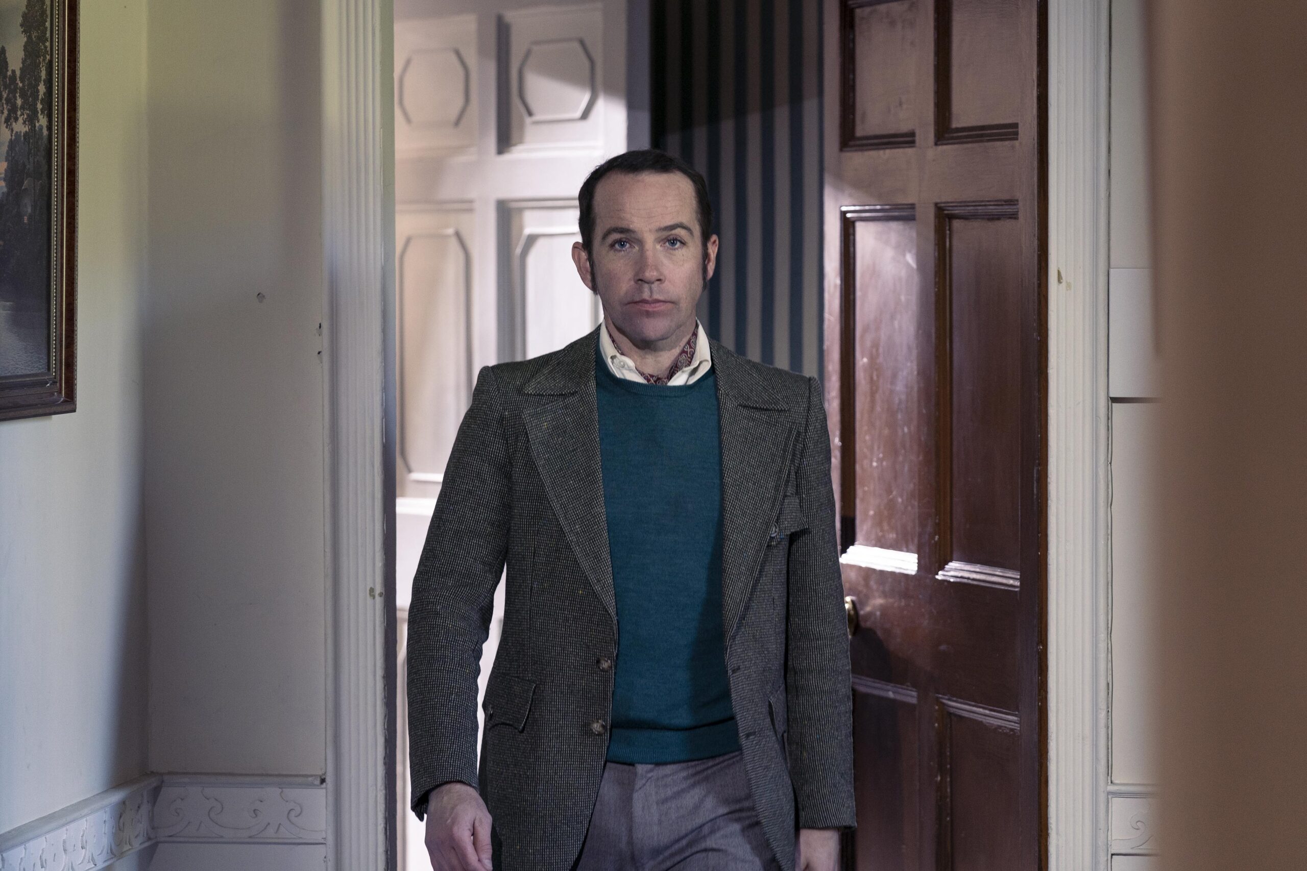 Julius Court walks through a door in a suit in Dalgliesh