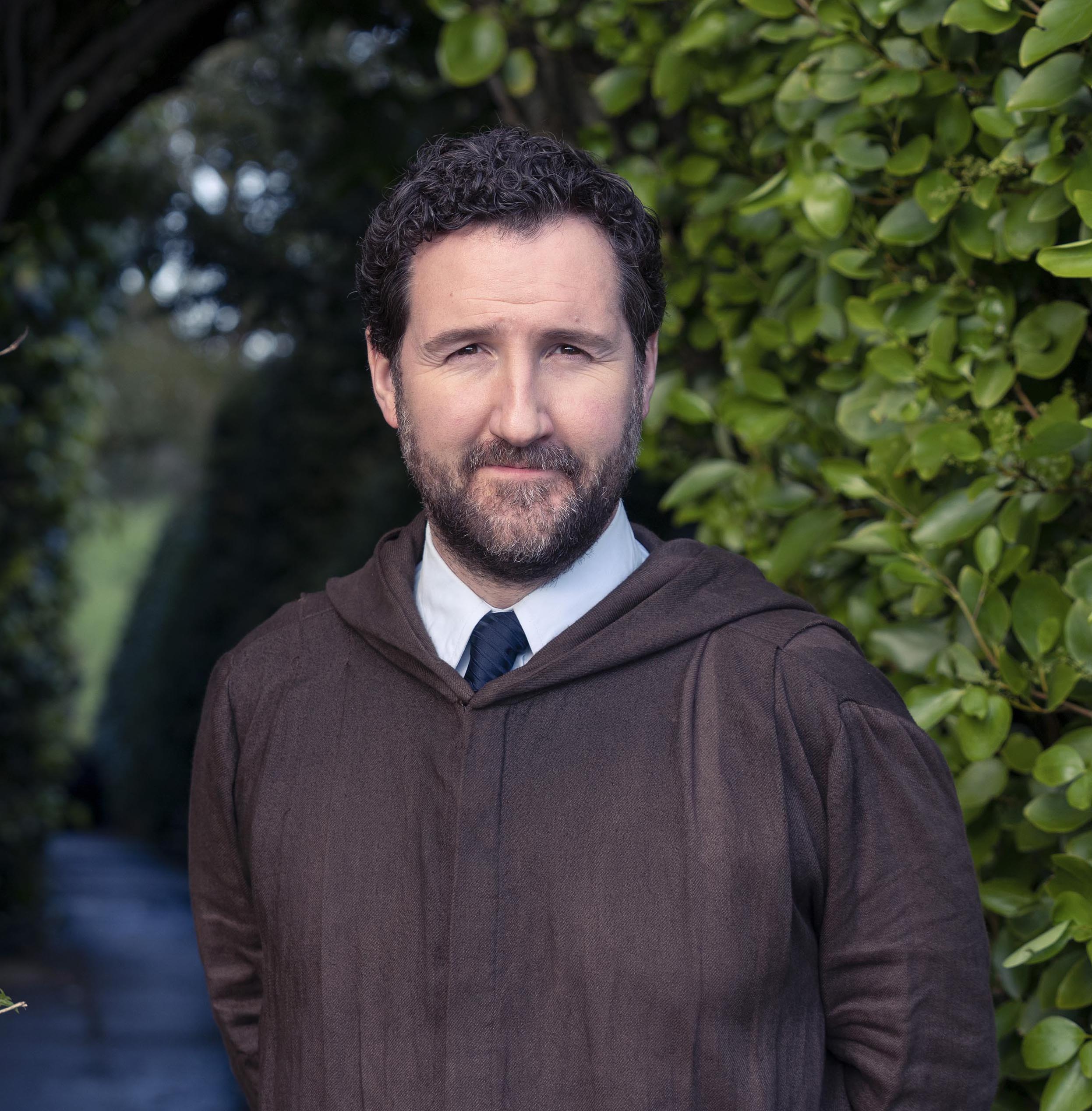 Dr Hewson smiles in brown robes in Dalgliesh