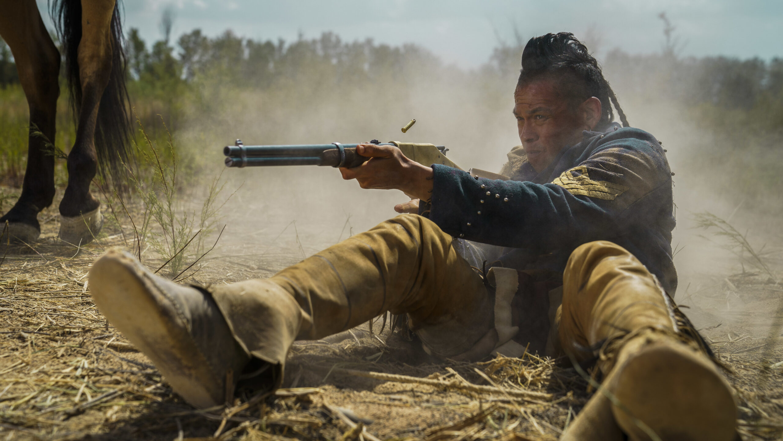 Eli sits in sand shooting a gun