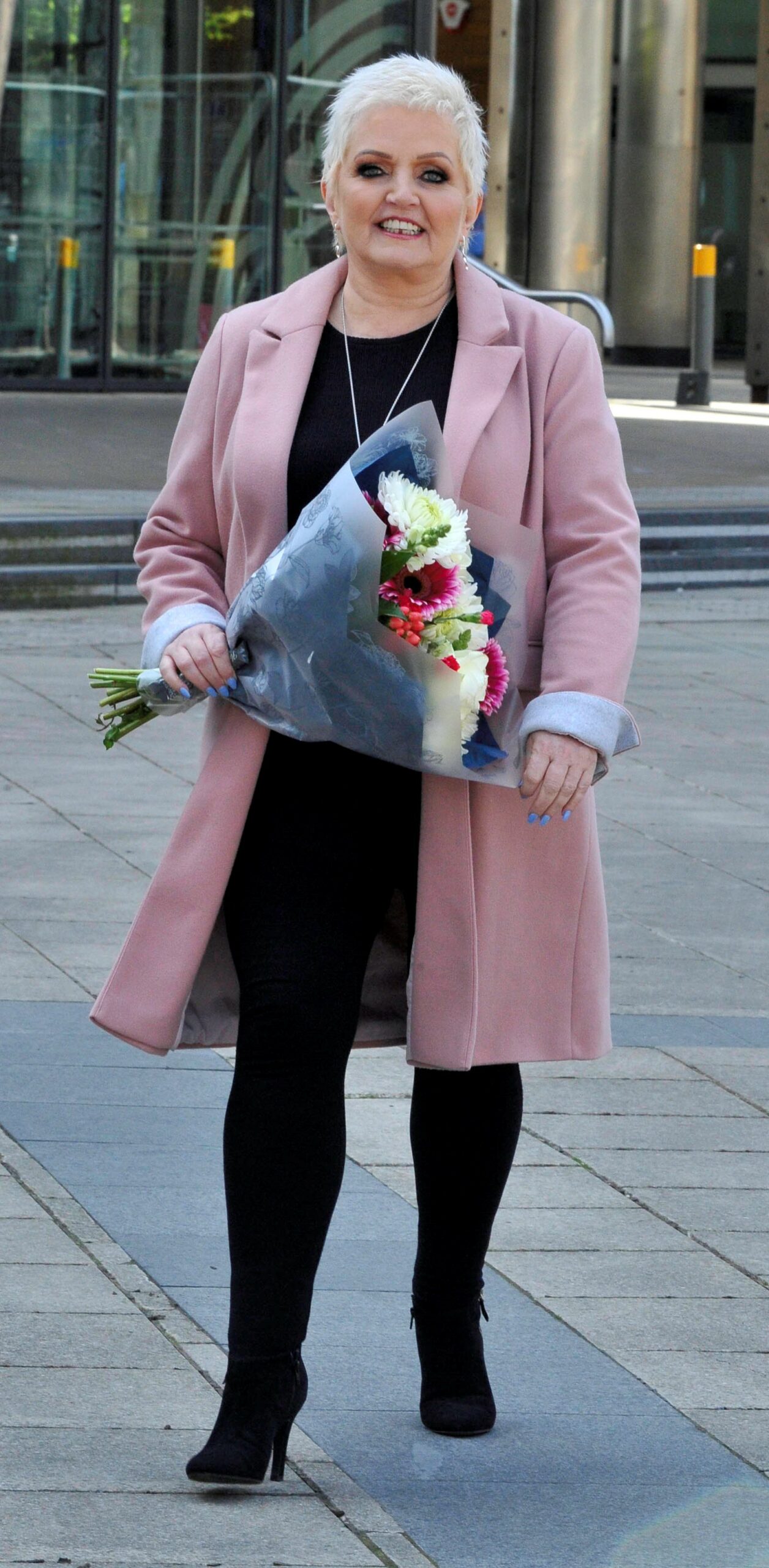 Linda Nolan smiling with flowers in pink coat