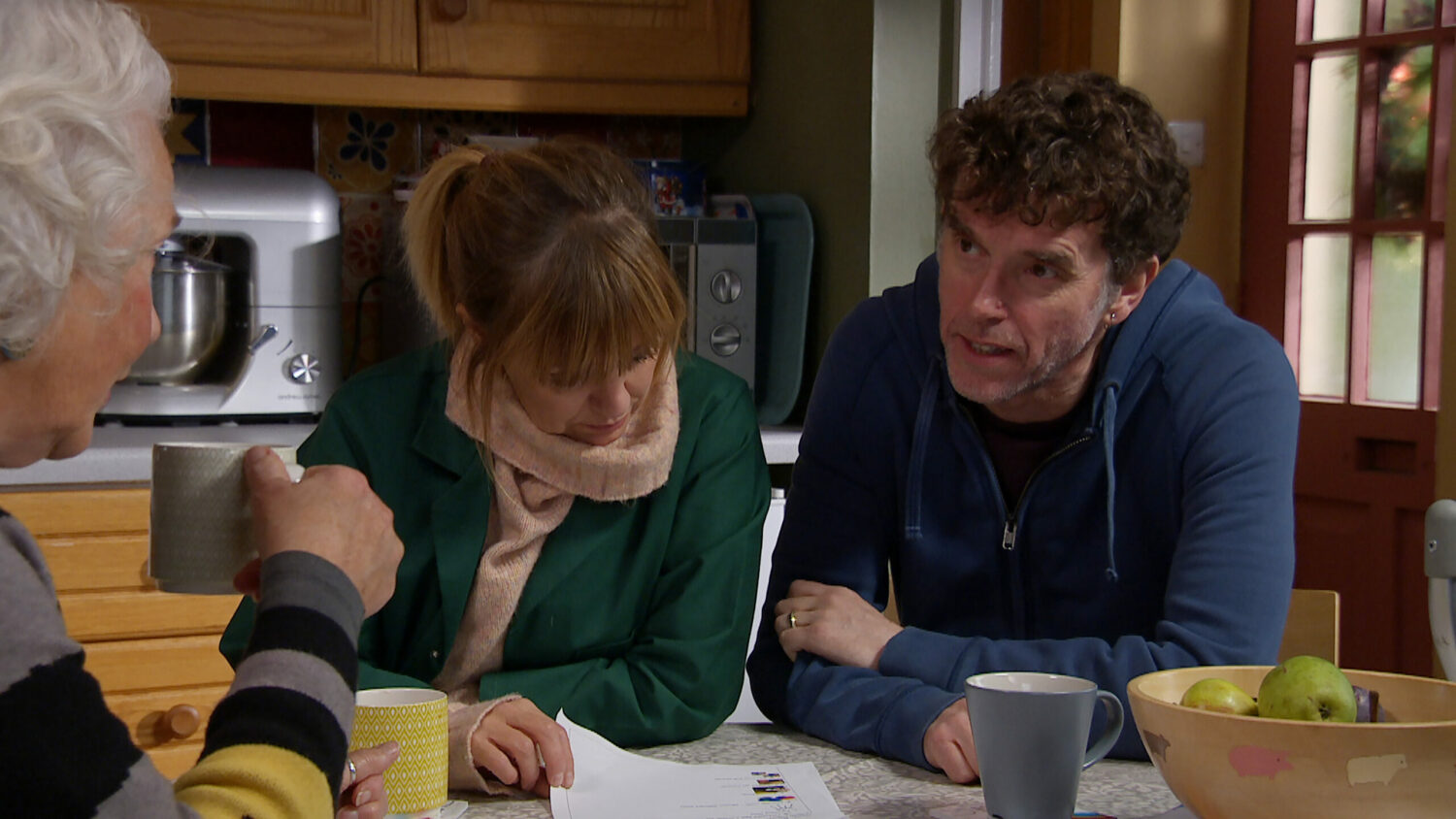 Rhona looks at a piece of paper as Marlon looks at Mary 