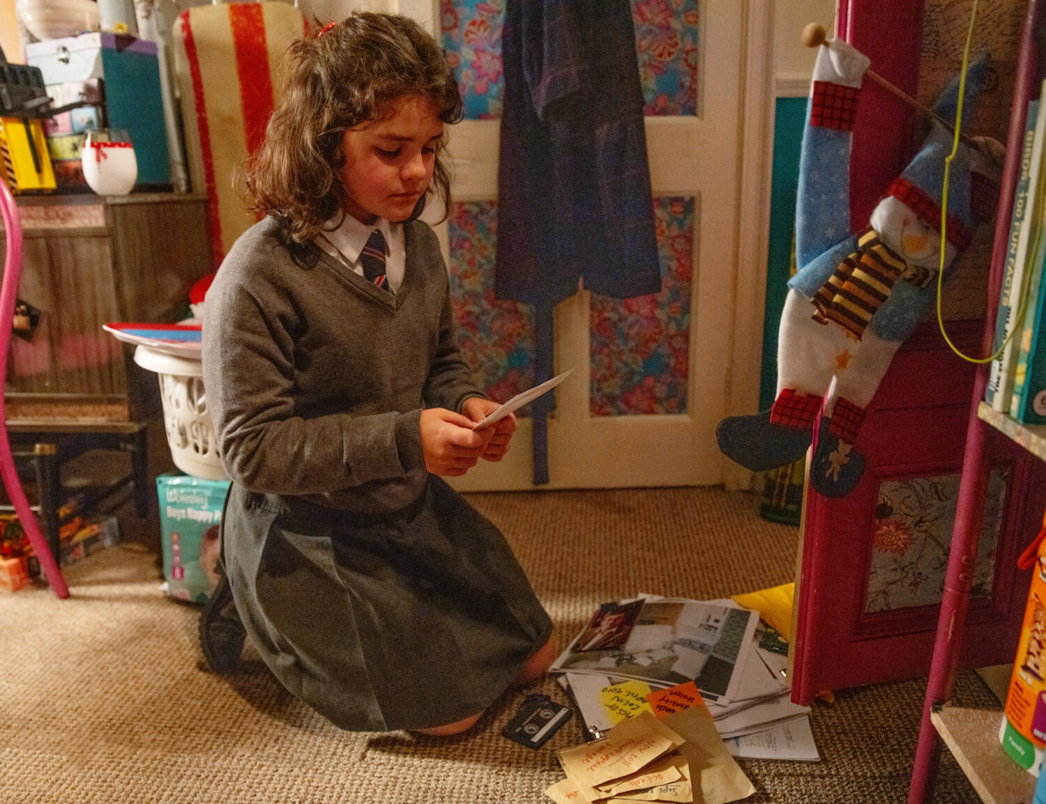 Hope kneeling by a pile of papers and letters, written by John Stape on Corrie