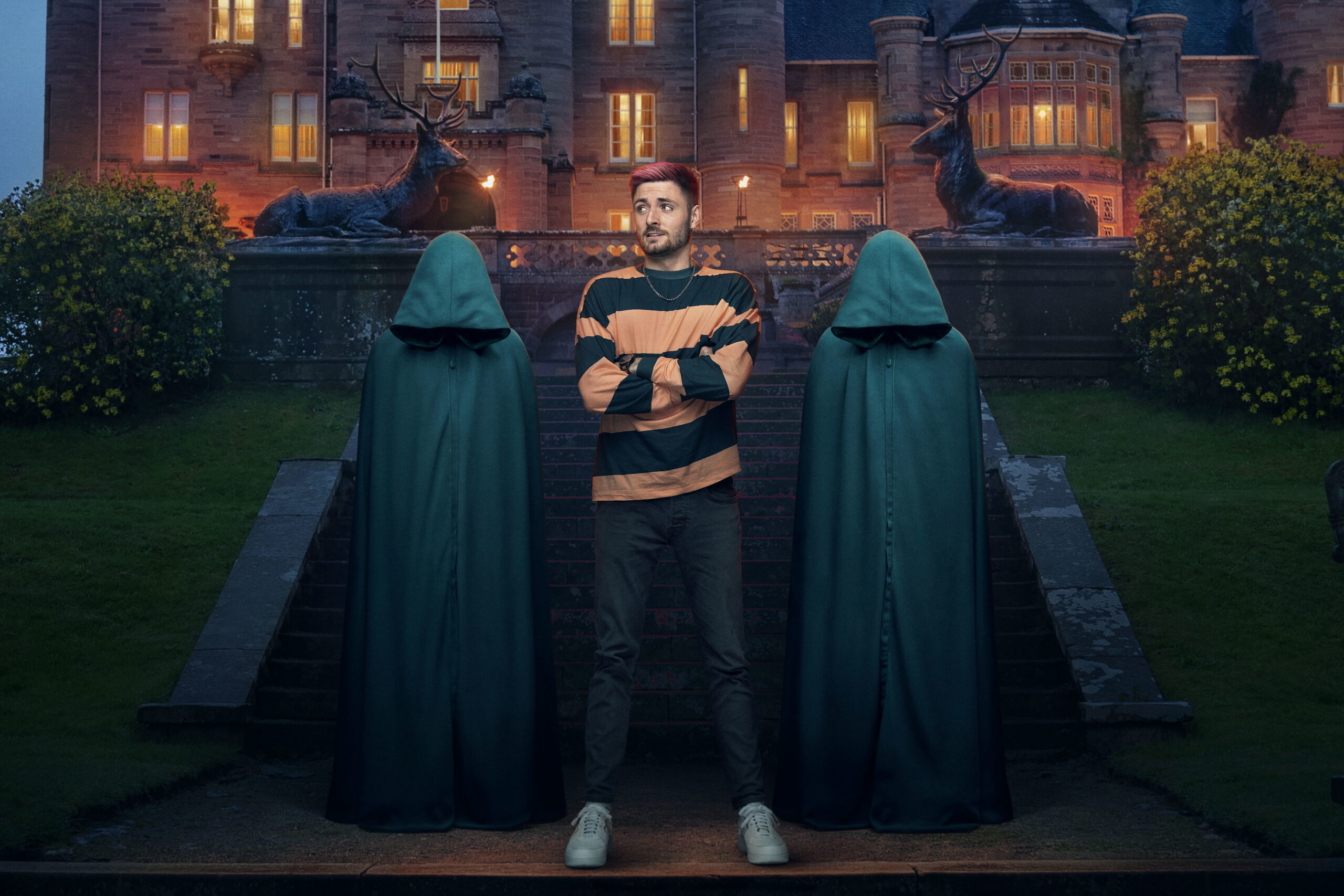 Tom folds his arms between the two hooded figures