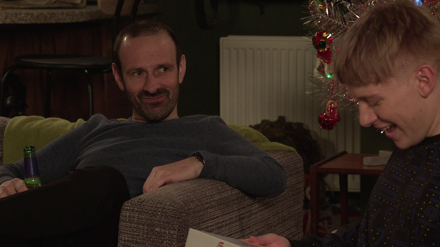 Griff smiling creepily while Max smiles happily, looking at his gift, on Coronation Street
