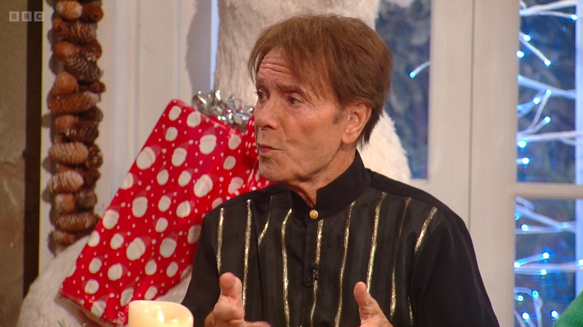 Cliff Richard talks animatedly on Saturday Kitchen in a black and gold striped grandad shirt