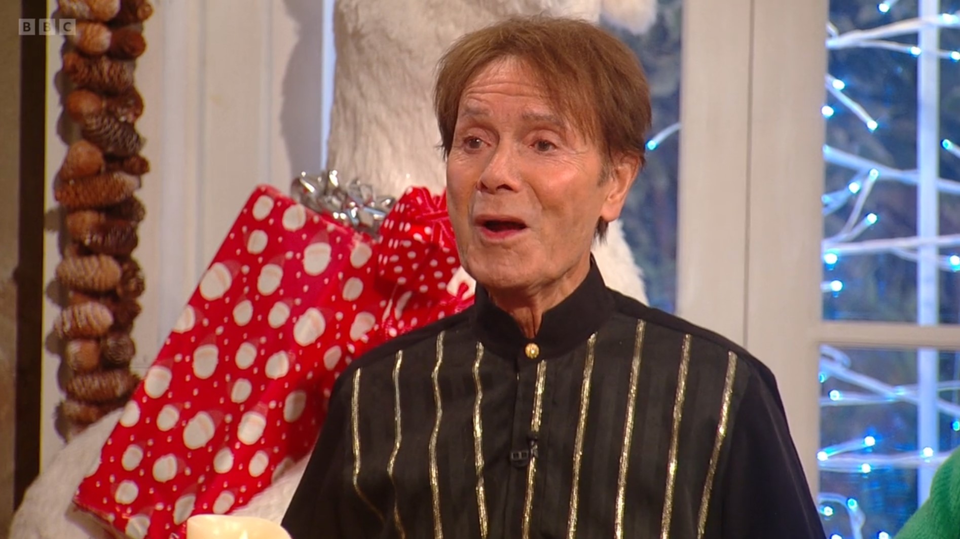 Cliff Richard talks animatedly on Saturday Kitchen in a black and gold striped grandad shirt