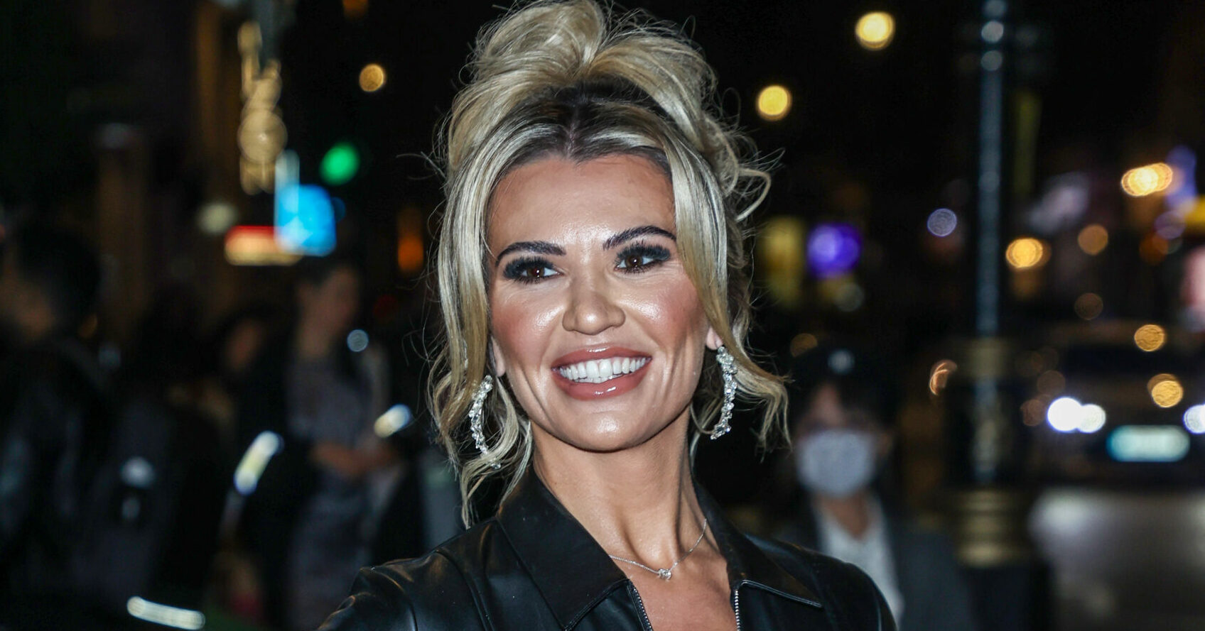 Christine McGuinness smiles with hand on her hip in black leather mini-dress