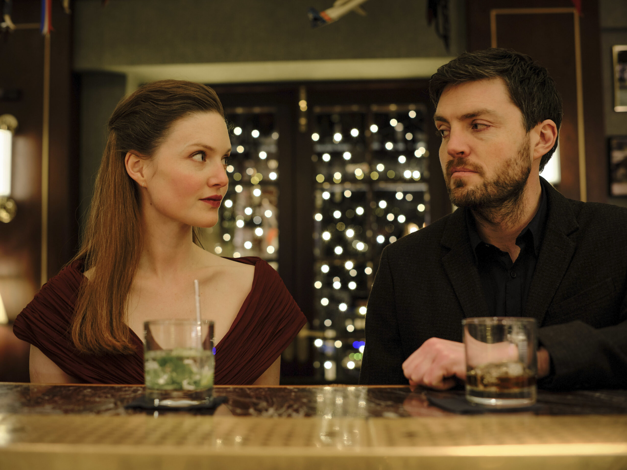 Robin and Cormoran Strike smile at each other at a bar