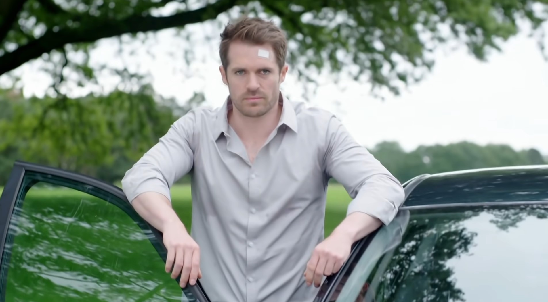 Laurie Shelby in Hollyoaks lean on the car door looking menacing with a cut on his head