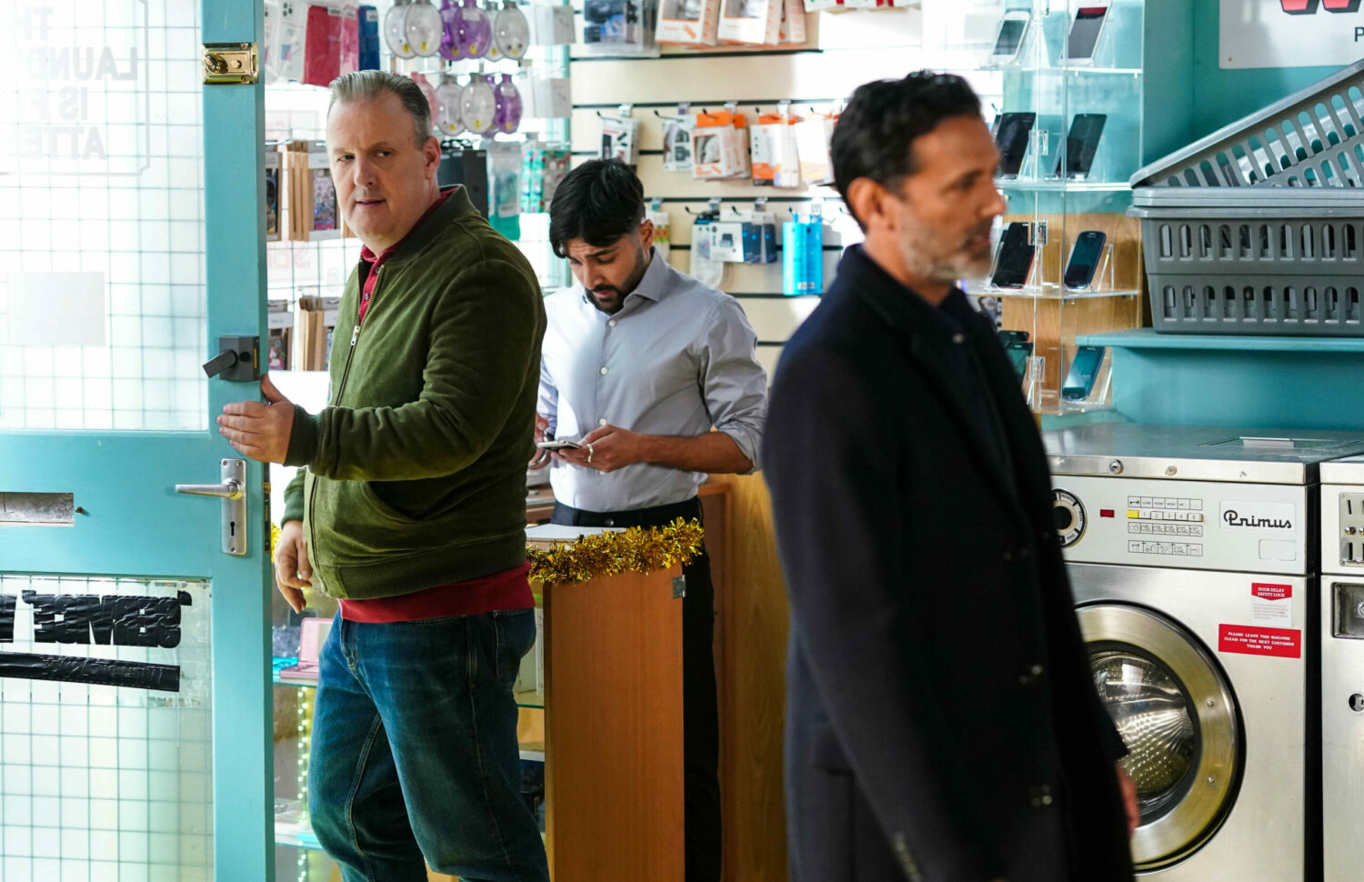 Nish, his back turned on Harvey, who is saying something unpleasant to him on EastEnders