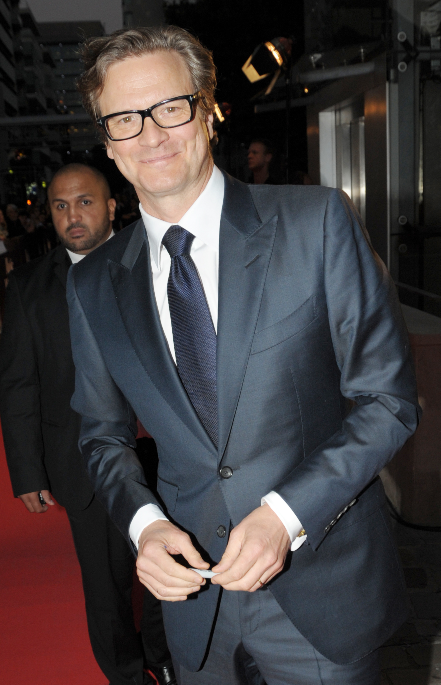 Colin Firth smiling on the red carpet wearing glasses