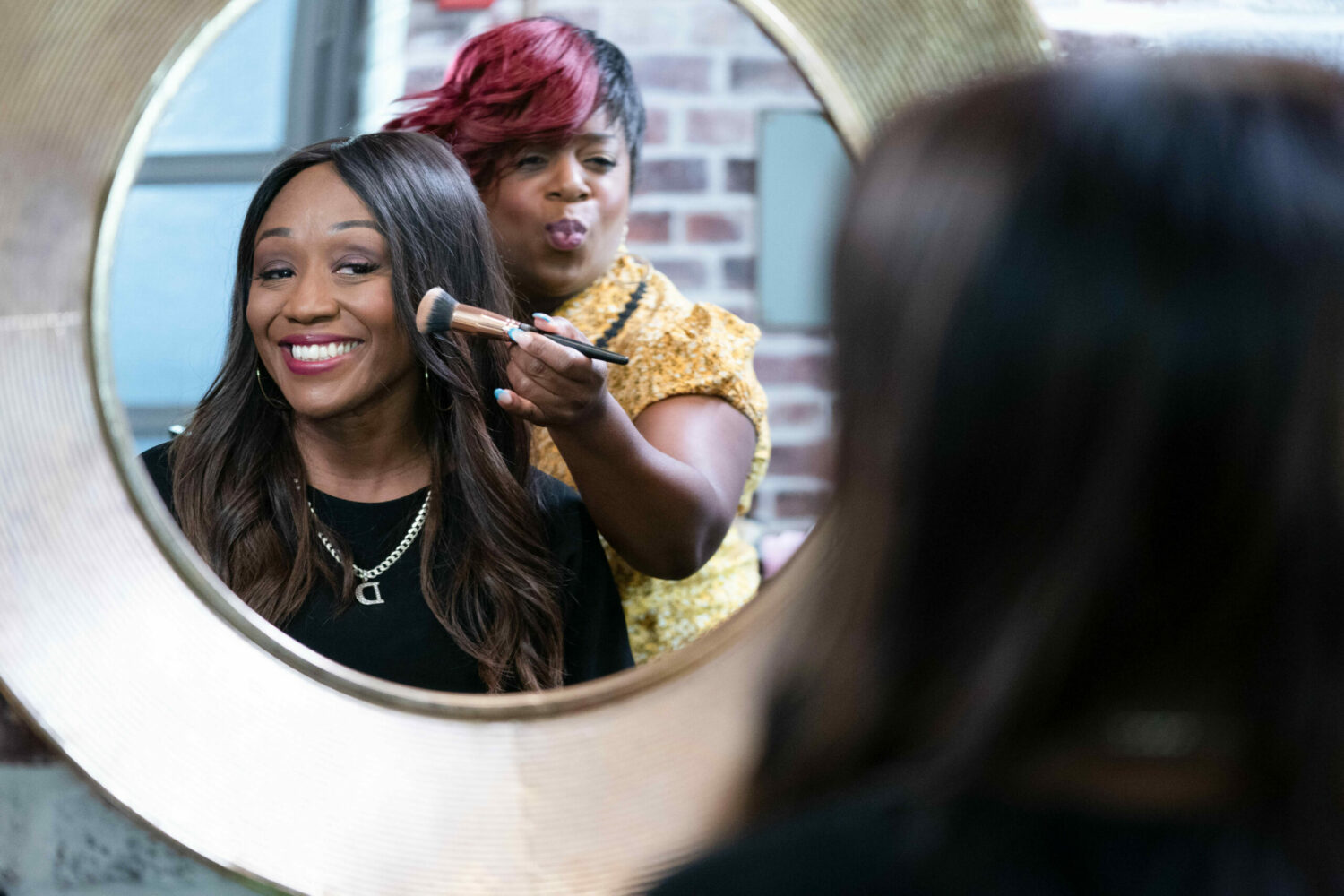 EastEnders' Denise is smiling into a mirror as Kim pouts and holds a makeup brush to her face