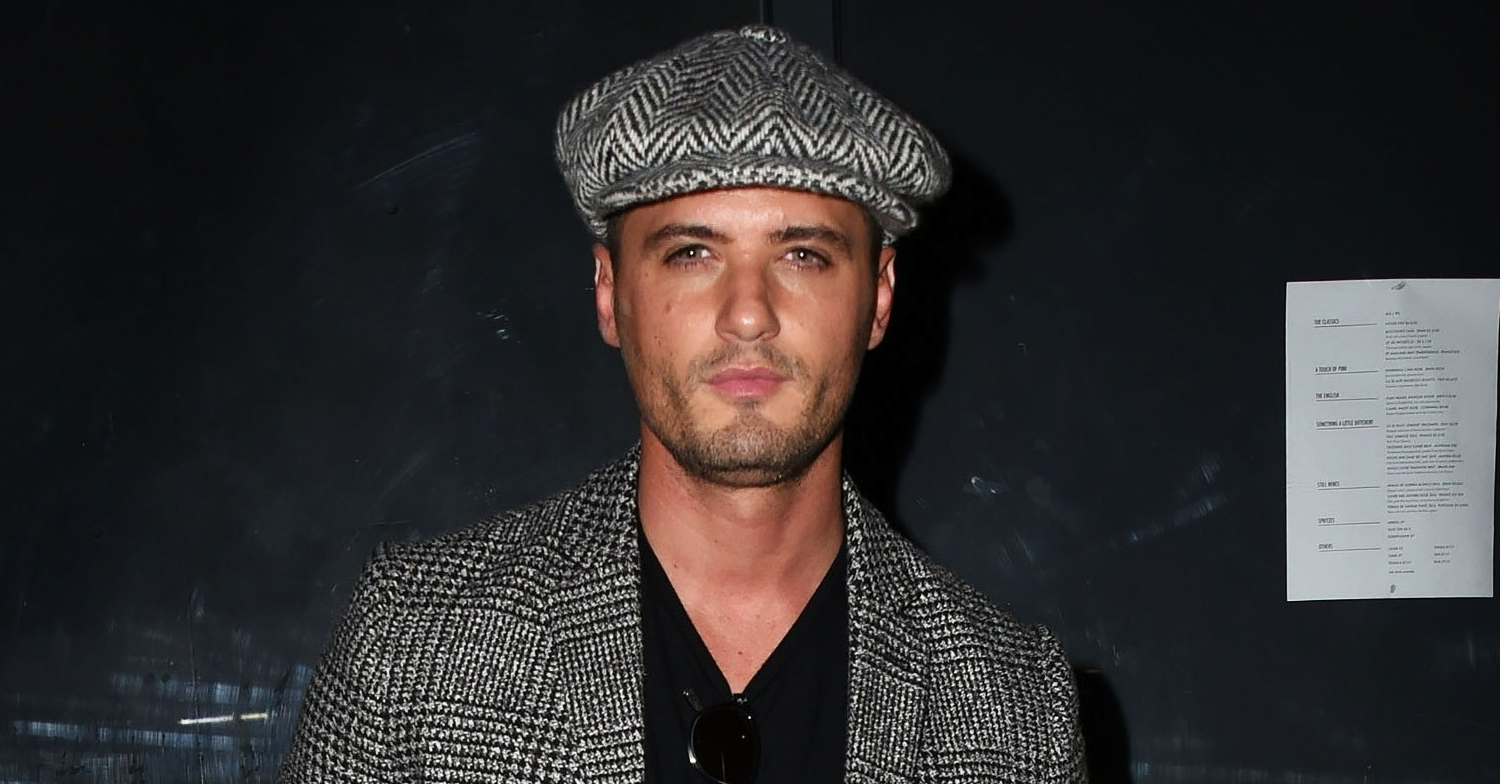 EastEnders star Fabrizio Santino is wearing a flat cap and posing at a press event