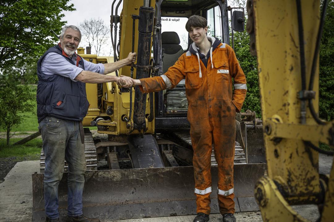 Clive and Reuben shake hands next to a digger on Our Yorkshire Farm
