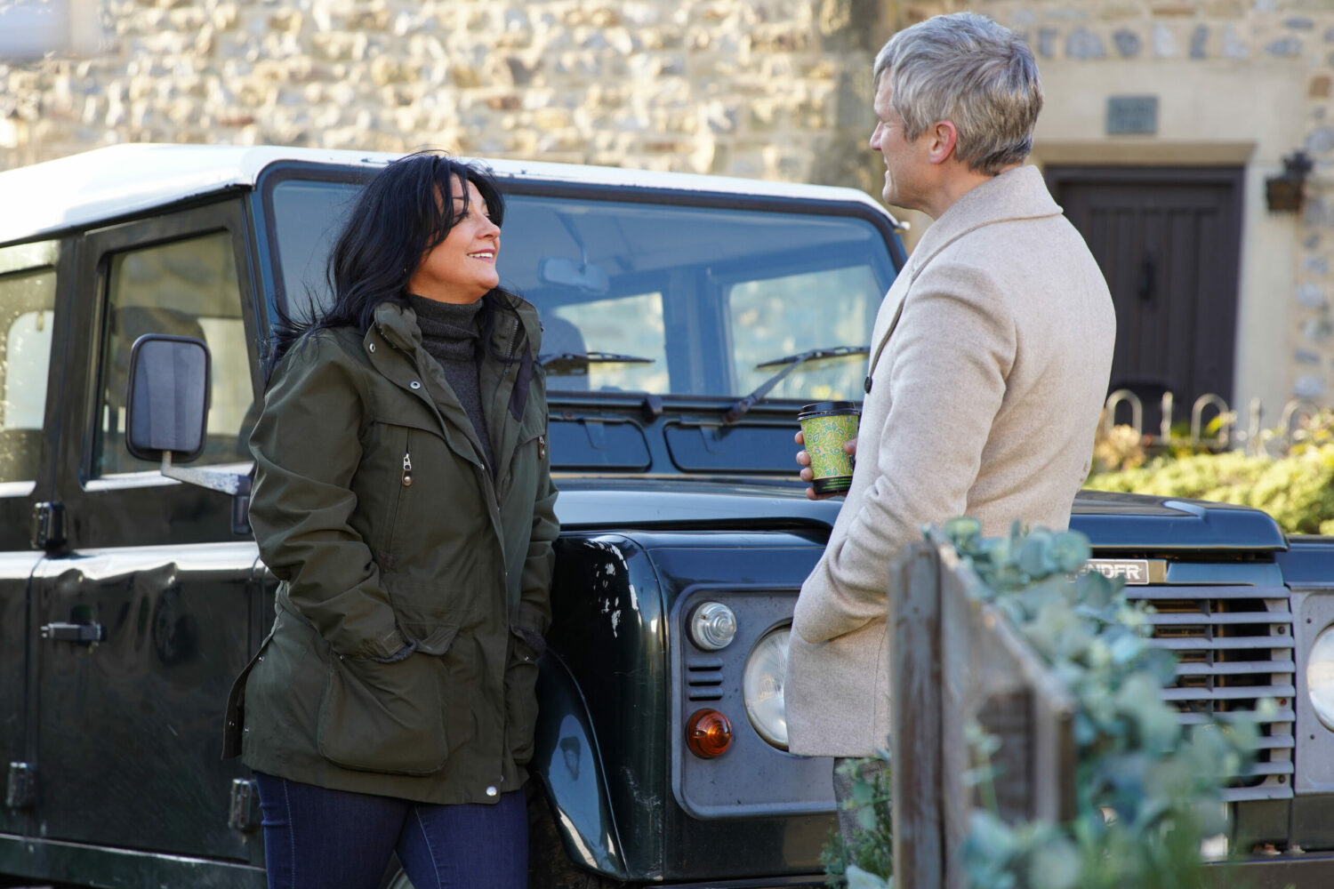 Moira smiles at Caleb while leaning on a Landrover in Emmerdale