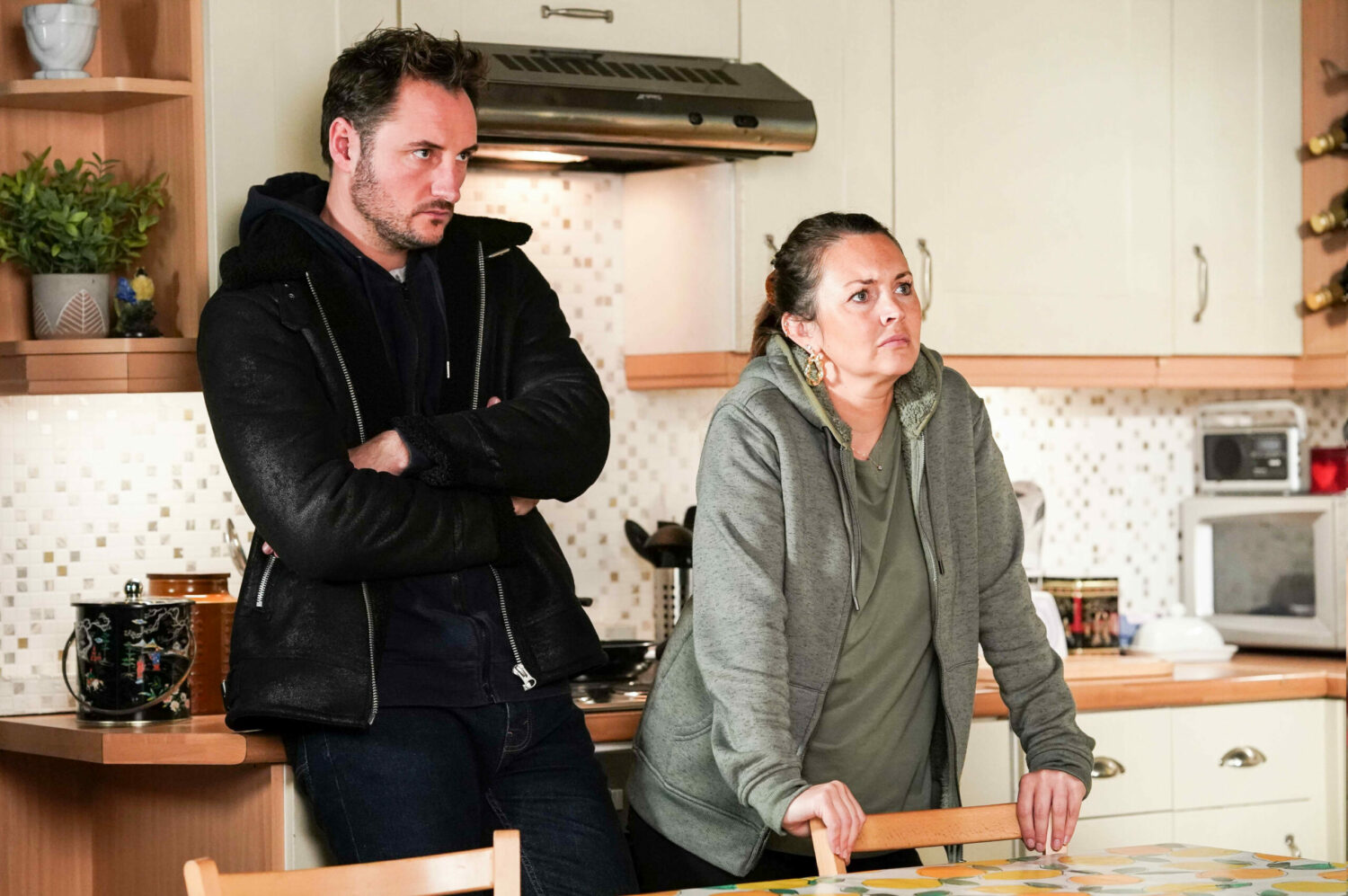Martin Fowler stands with his arms folded and Stacey Slater leans on a chair looking annoyed