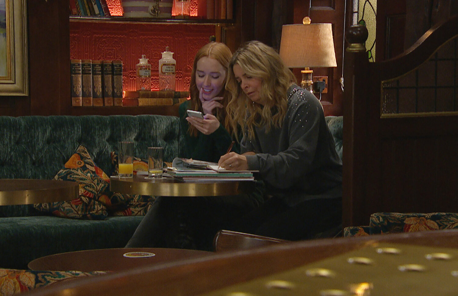 Chloe and Charity look conspiratorial as they look at phones and make notes
