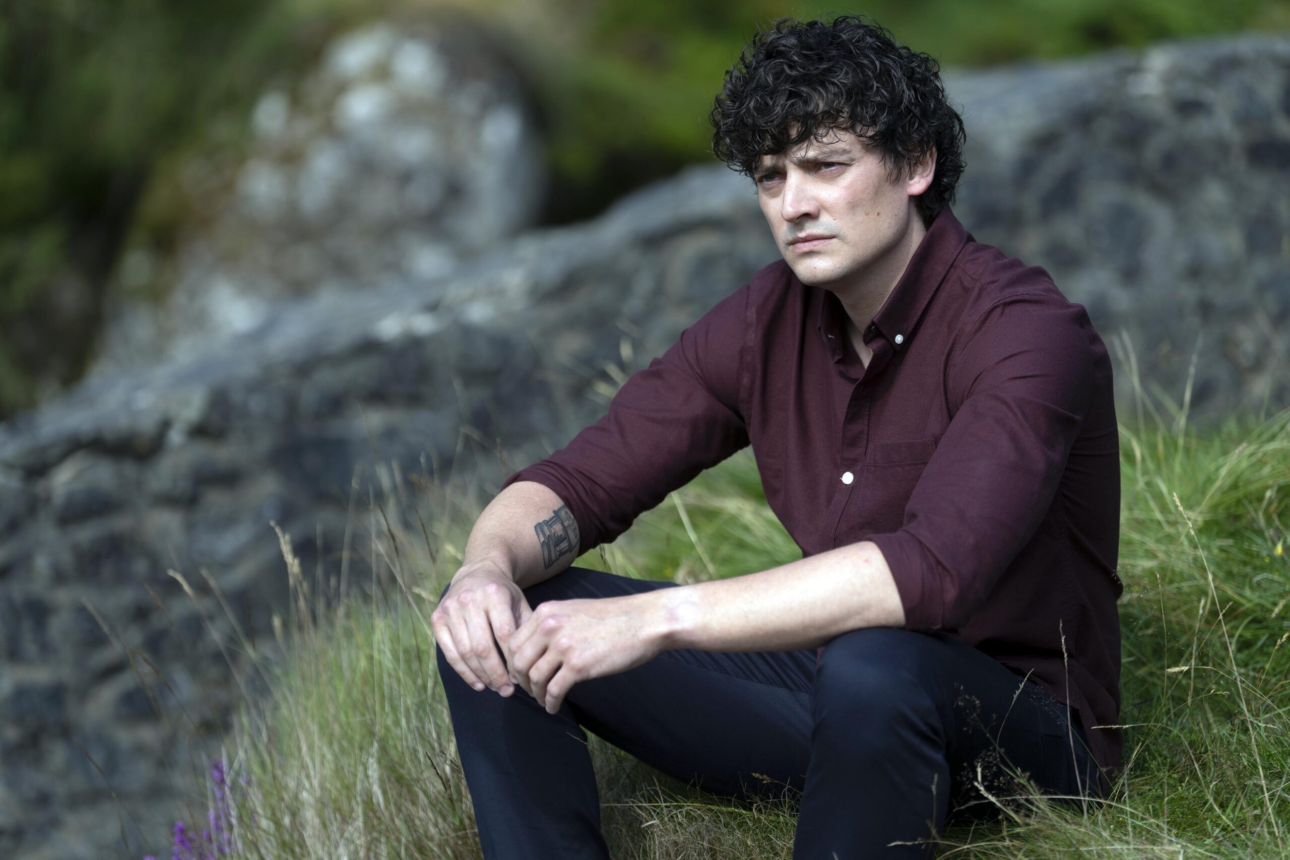Aneurin Barnard sitting in the grass in The Catch