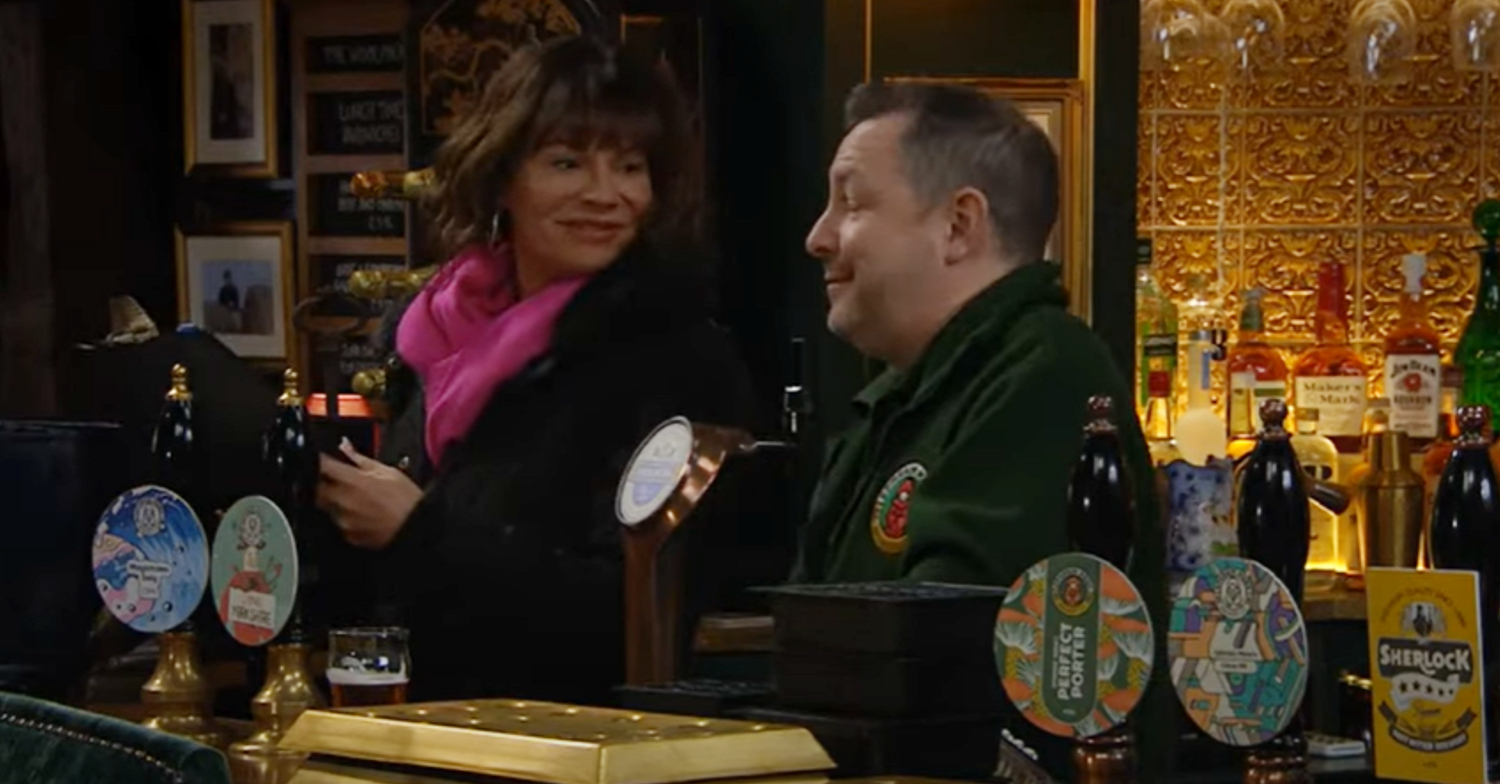 Emmerdale's Chas is smiling at Kev the drayman behind the bar