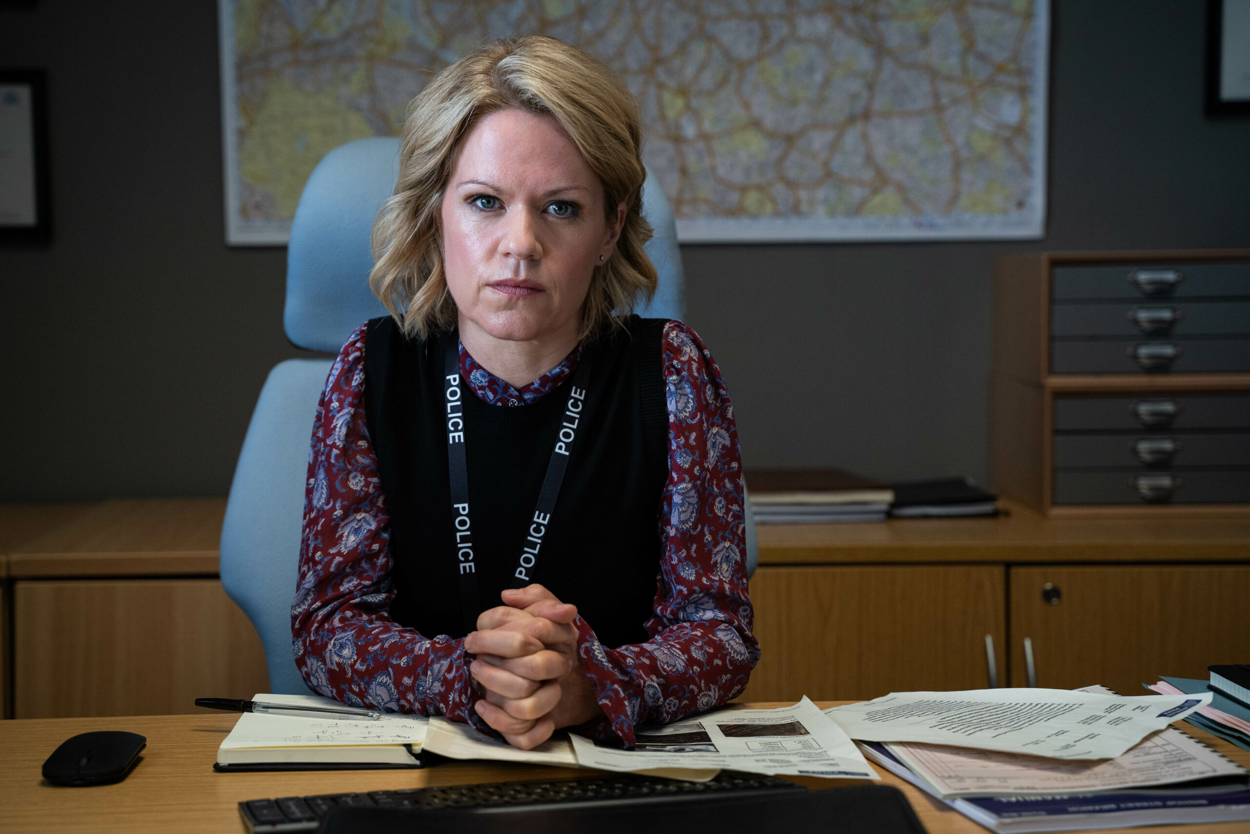 Jess sits at desk and smiles in Unforgotten
