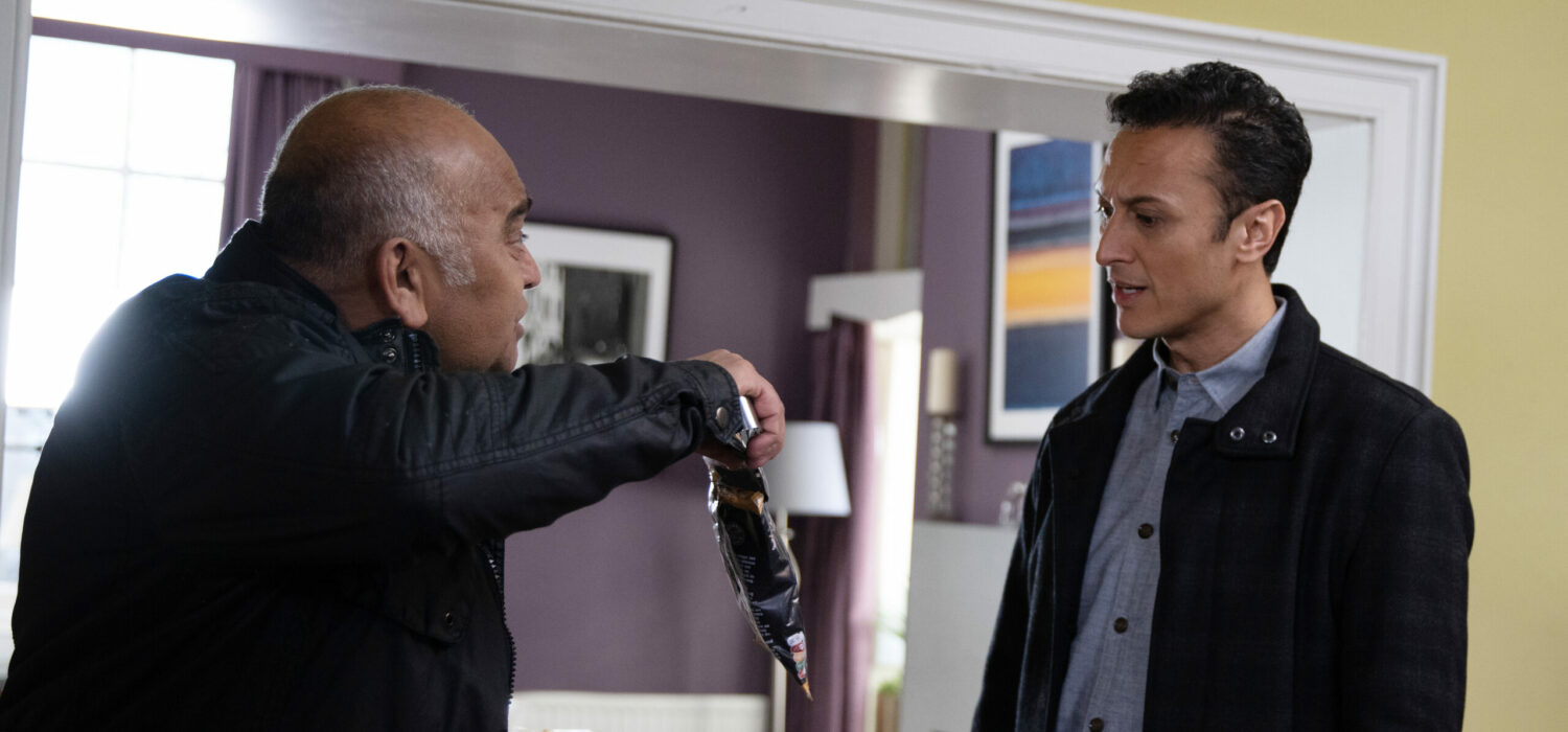 Rishi frantically holds up a crisp packet as Jai looks confused in Emmerdale