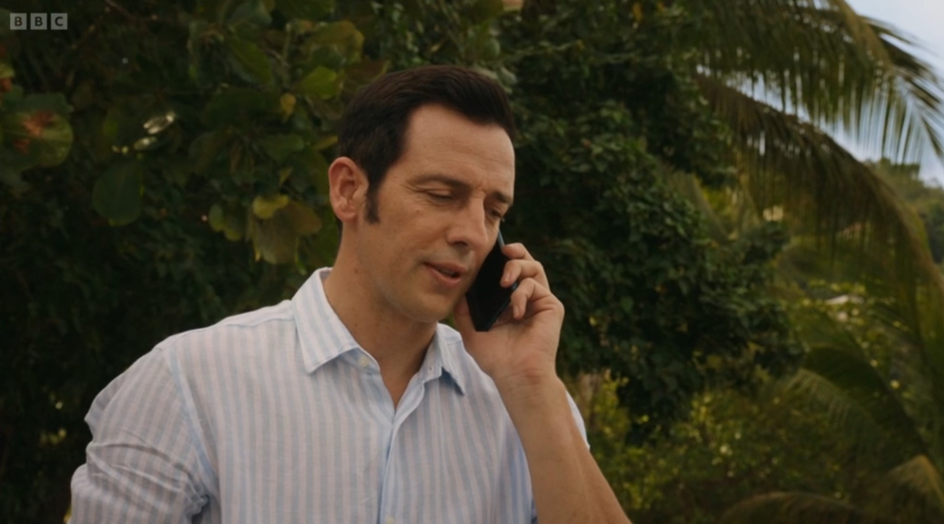 Neville Parker in Death in Paradise makes a phone call on the beach