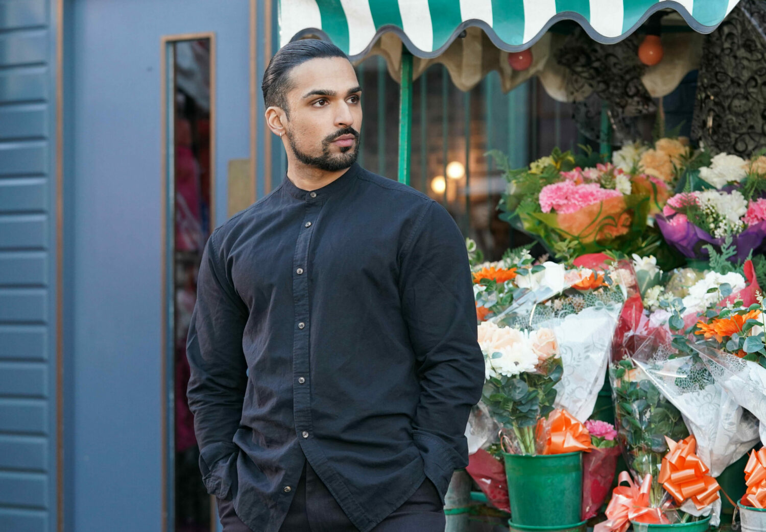 Ravi is outside the flower stall with his hands in his pockets