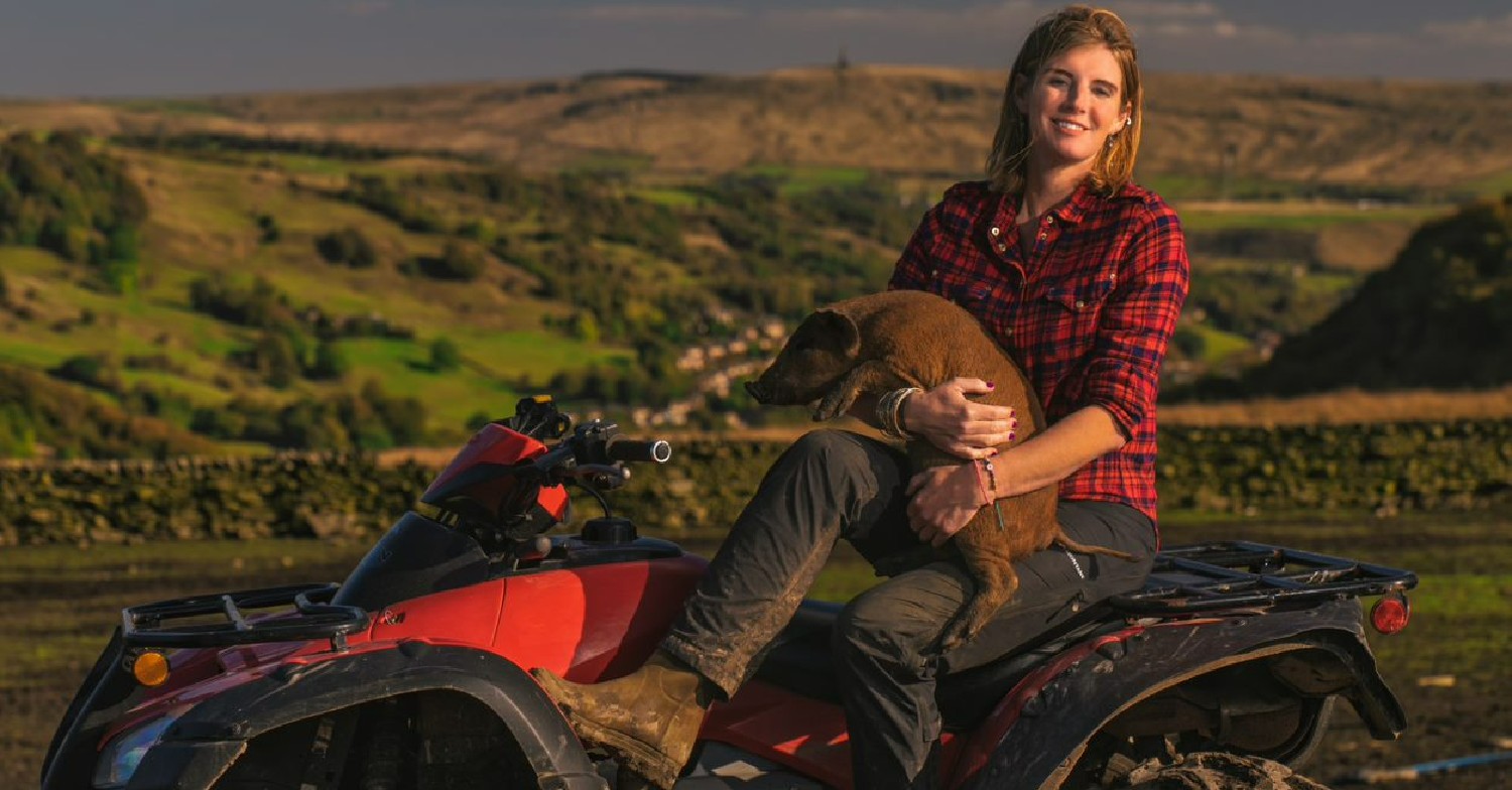 Amanda Owen holding a pig while sitting on a tractor