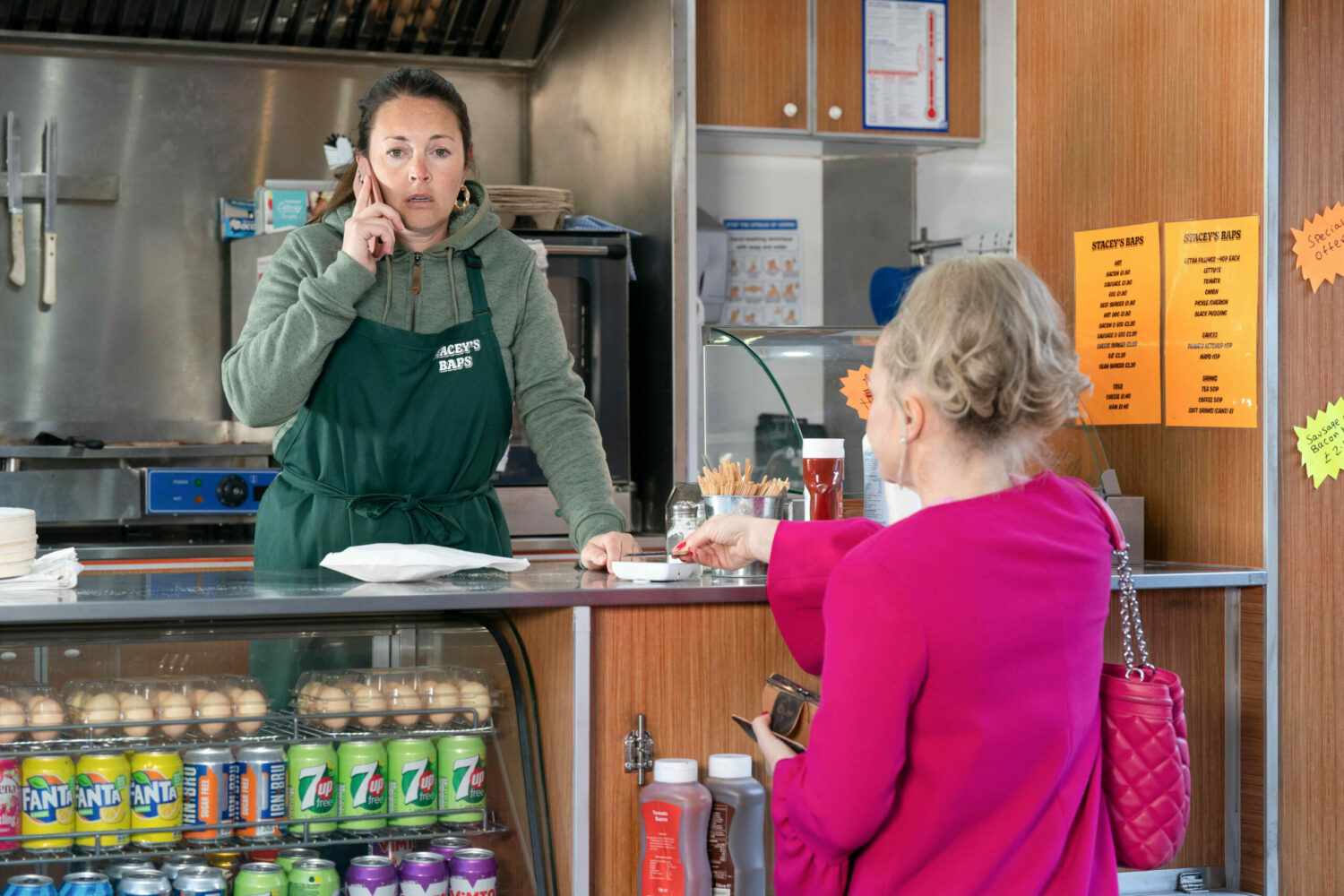 Stacey takes a phone call as Linda pays her money in EastEnders
