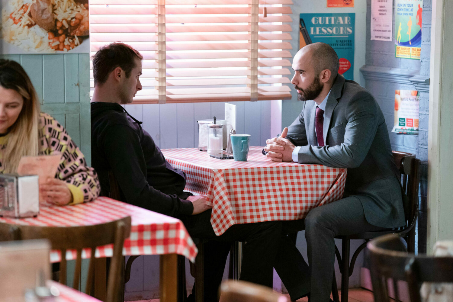 Ben talks to a plain clothes police officer in the cafe on EastEnders
