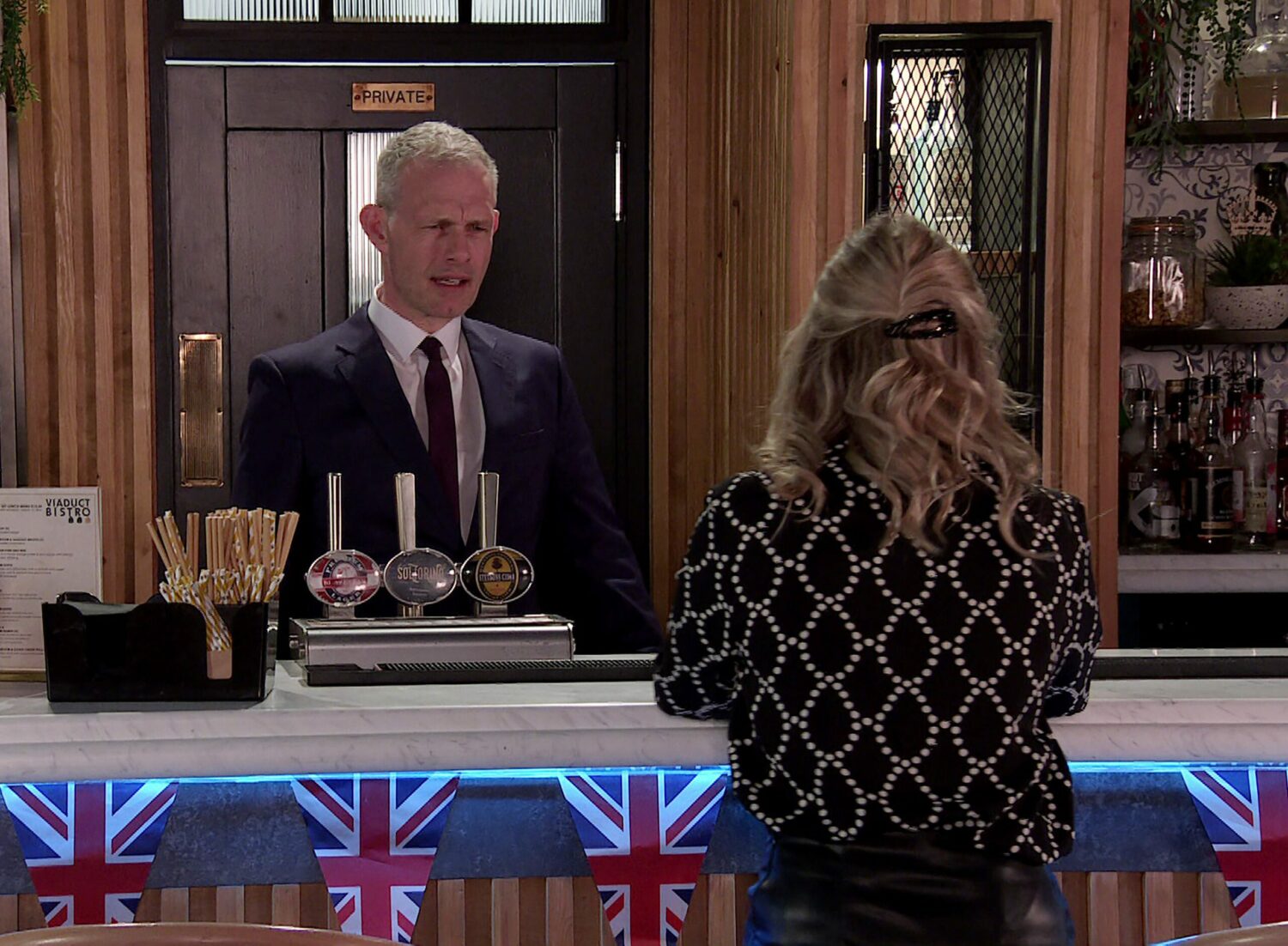 Coronation Street's Nick is behind the Bistro bar, looking at Sarah with concern
