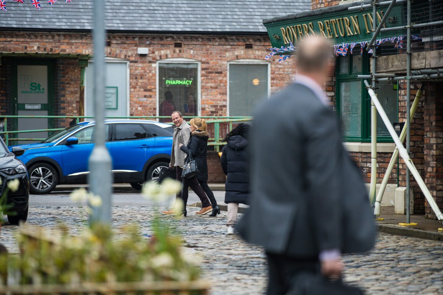 Owen and Jenny laugh outside the Rovers in Coronation Street as blurred Stephen looks on