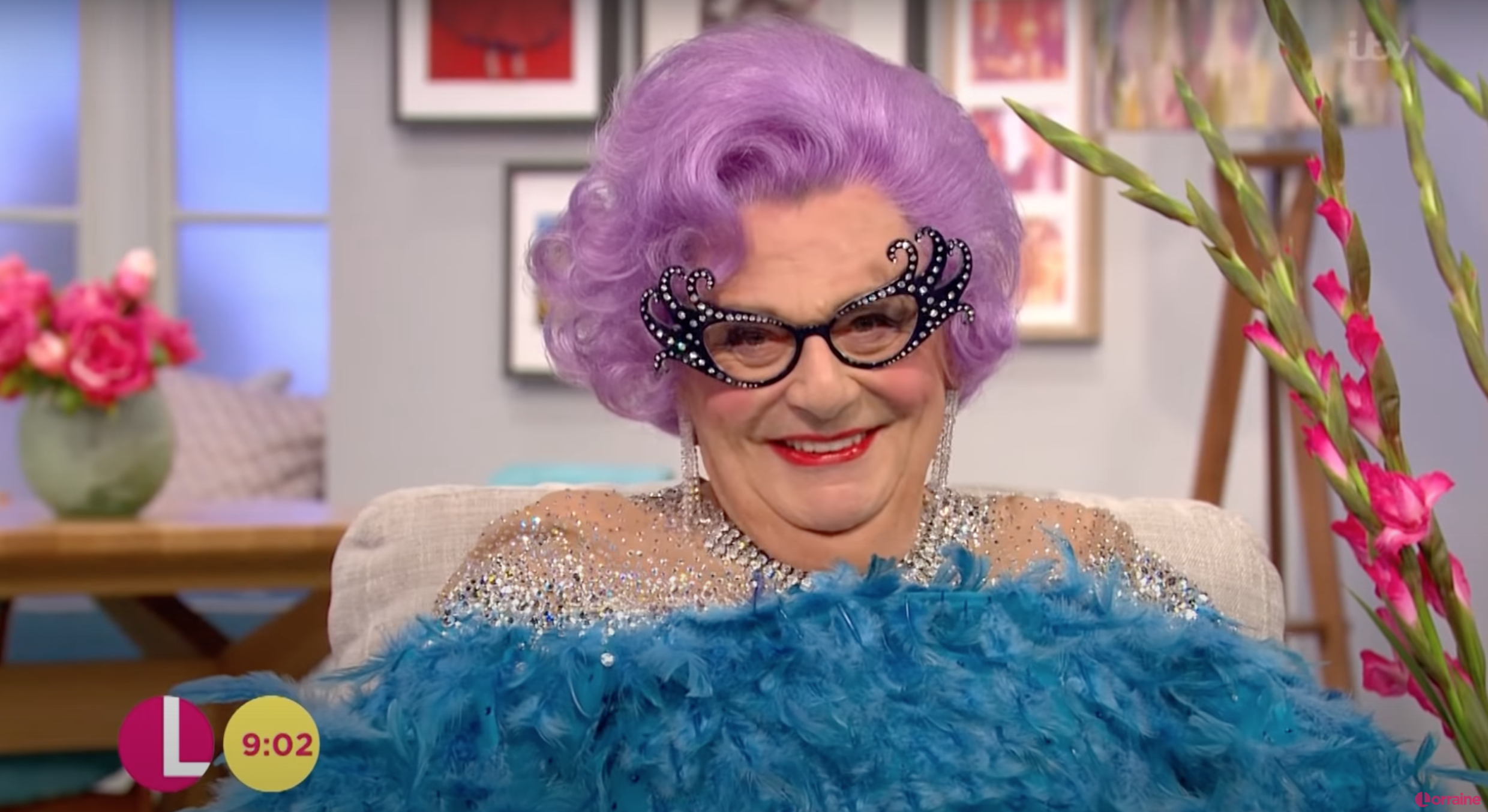 Dame Edna smiling wearing a pink wig