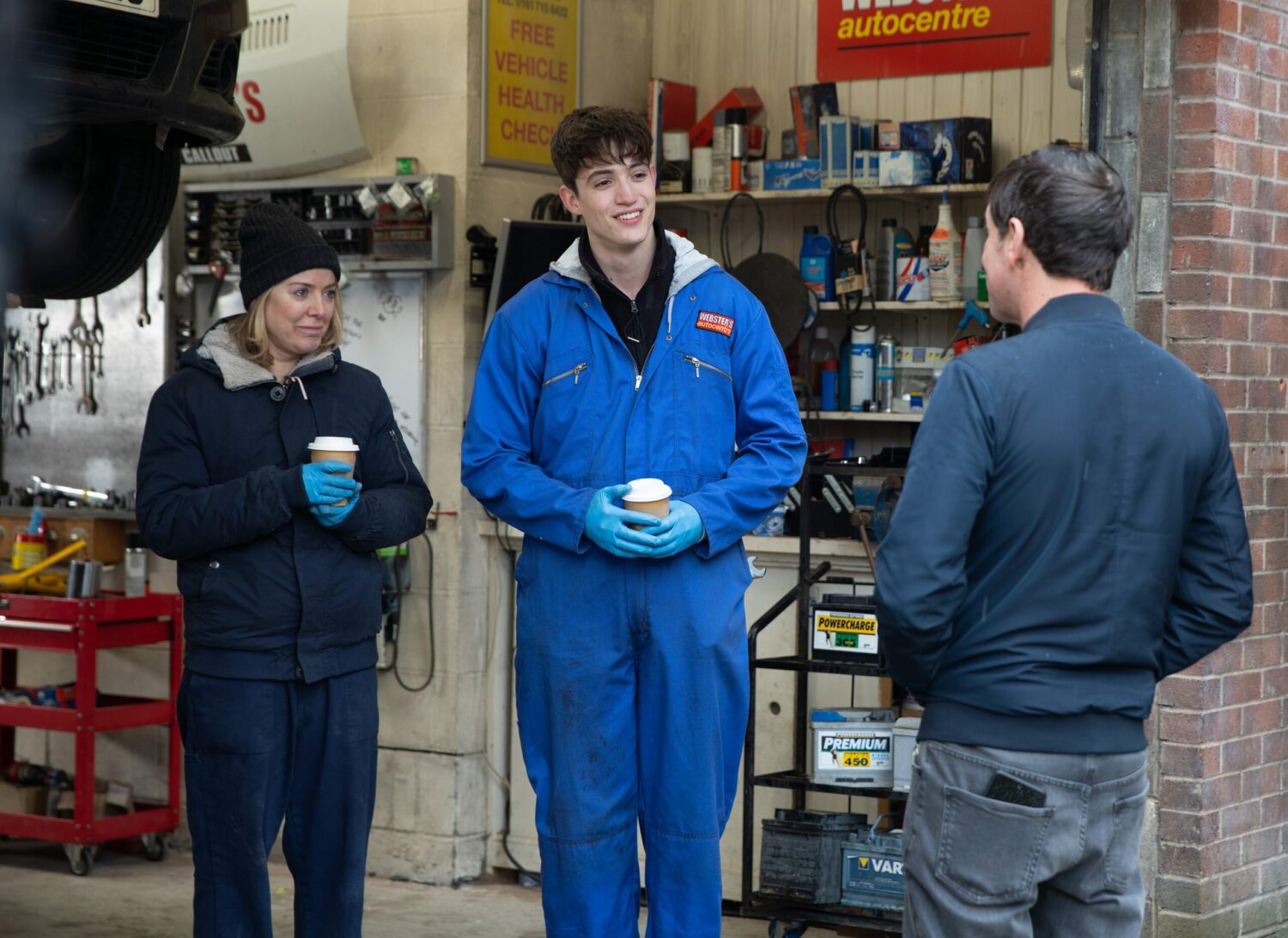 Abi and Aaron in Coronation Street smile as they hold coffee cups and talk to Eric