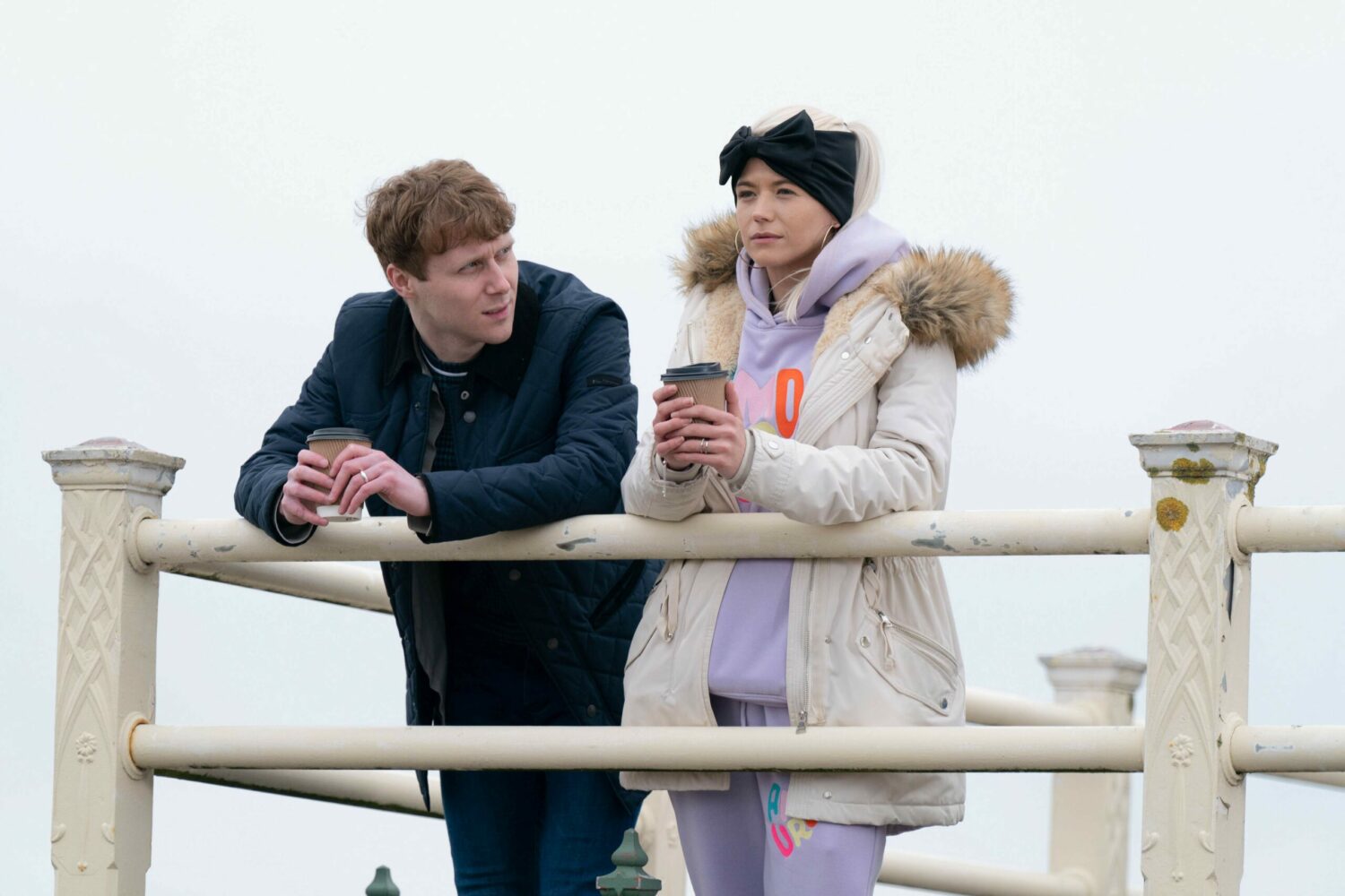 Jay and Lola drink coffees looking sad at the seaside in EastEnders