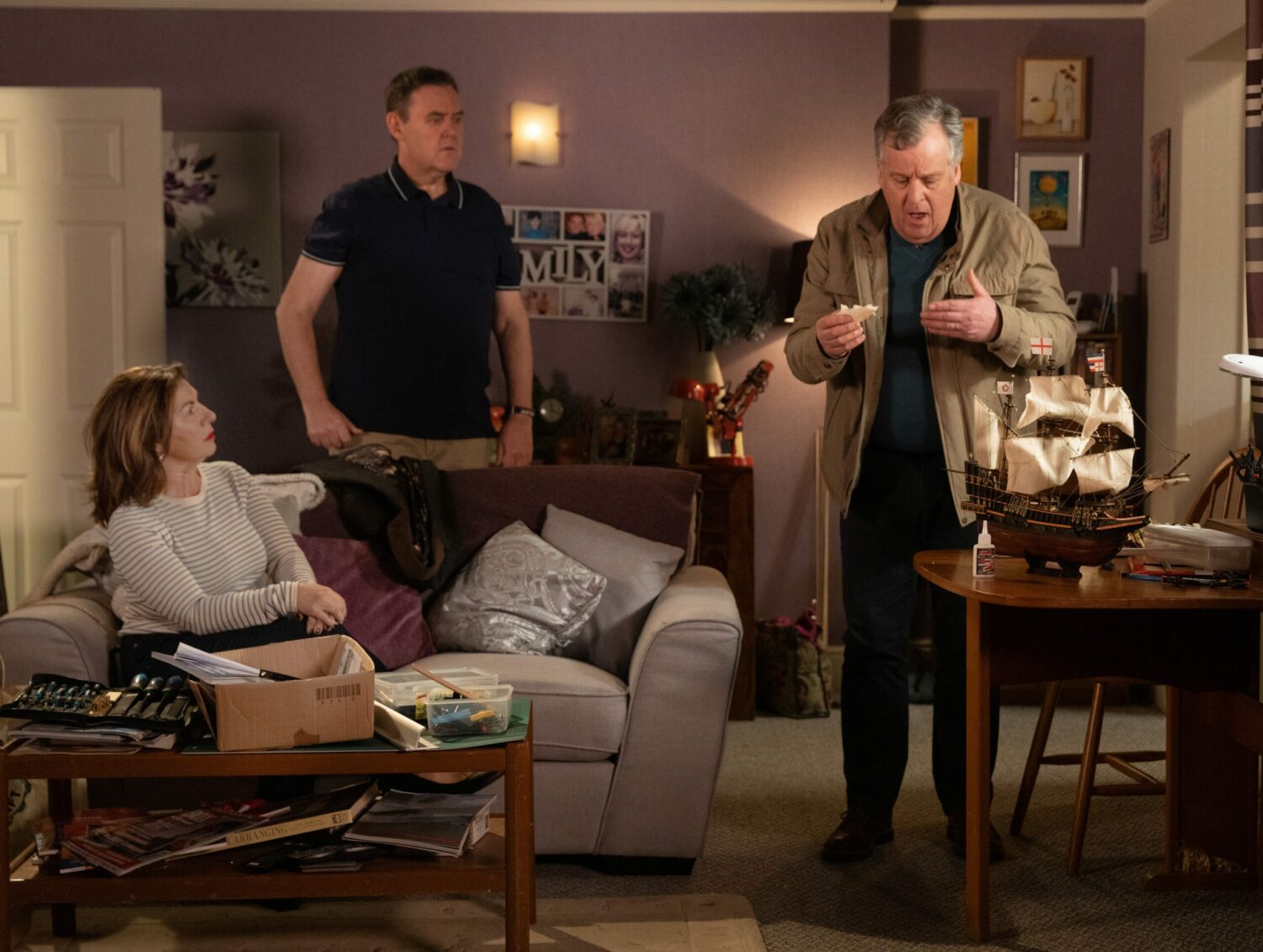 George in Corrie is shocked as Brian looks surprised at breaking the model ship. Isabella looks on pretending to be clueless.