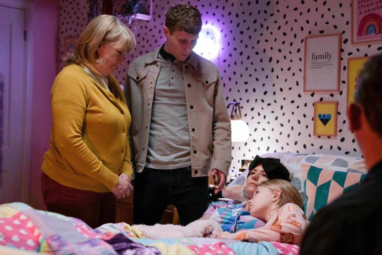 Reverend Mills in EastEnders offers Lola comfort as she lies in bed cuddling Lexi and Jay looks on