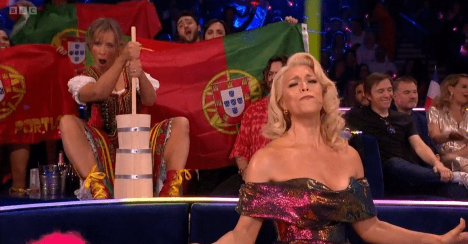 Mel Geidroyc pretending to churn butter behind host Hannah Waddingham during Eurovision final