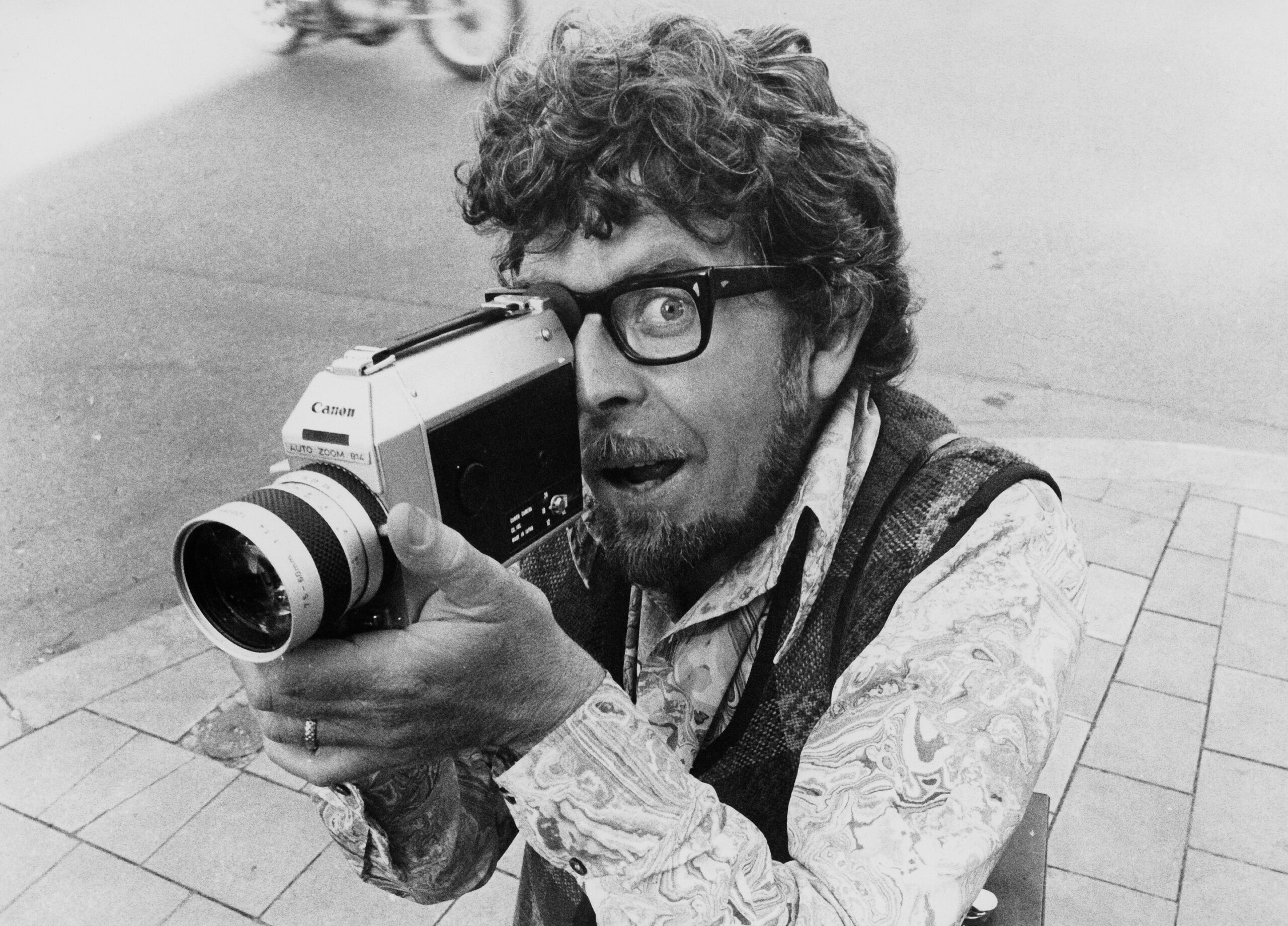 Rolf Harris holds a camera in black and white photo