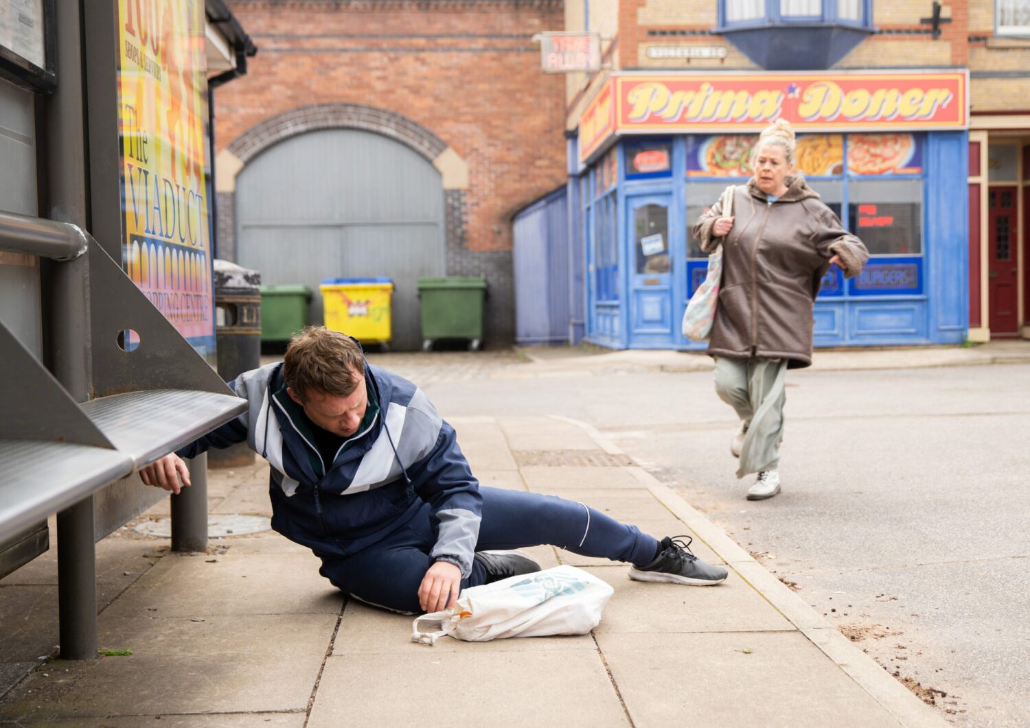 Coronation Street: Paul lies on the ground with his shopping bag as Bernie rushes over to help