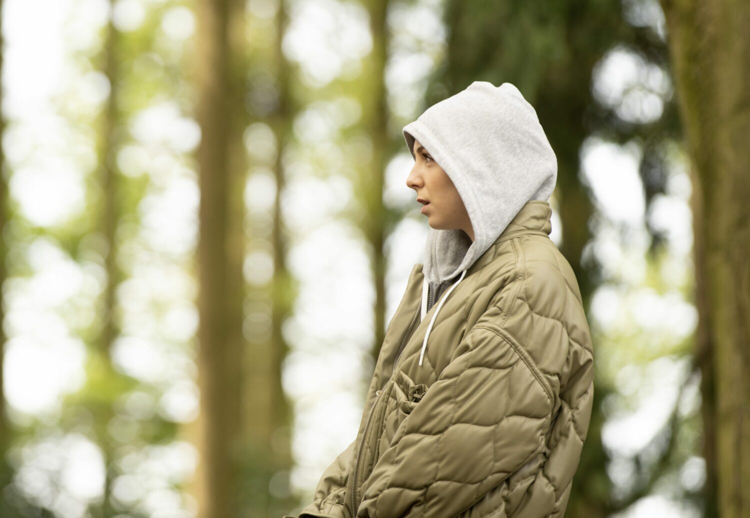 Belle Dingle with her hood up looks troubled in the woods