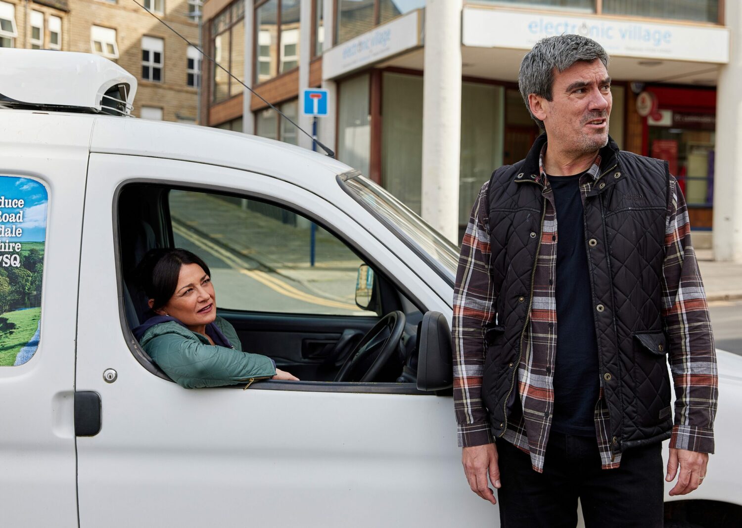 Moira in Emmerdale sits in the van while Cain looks round suspiciously